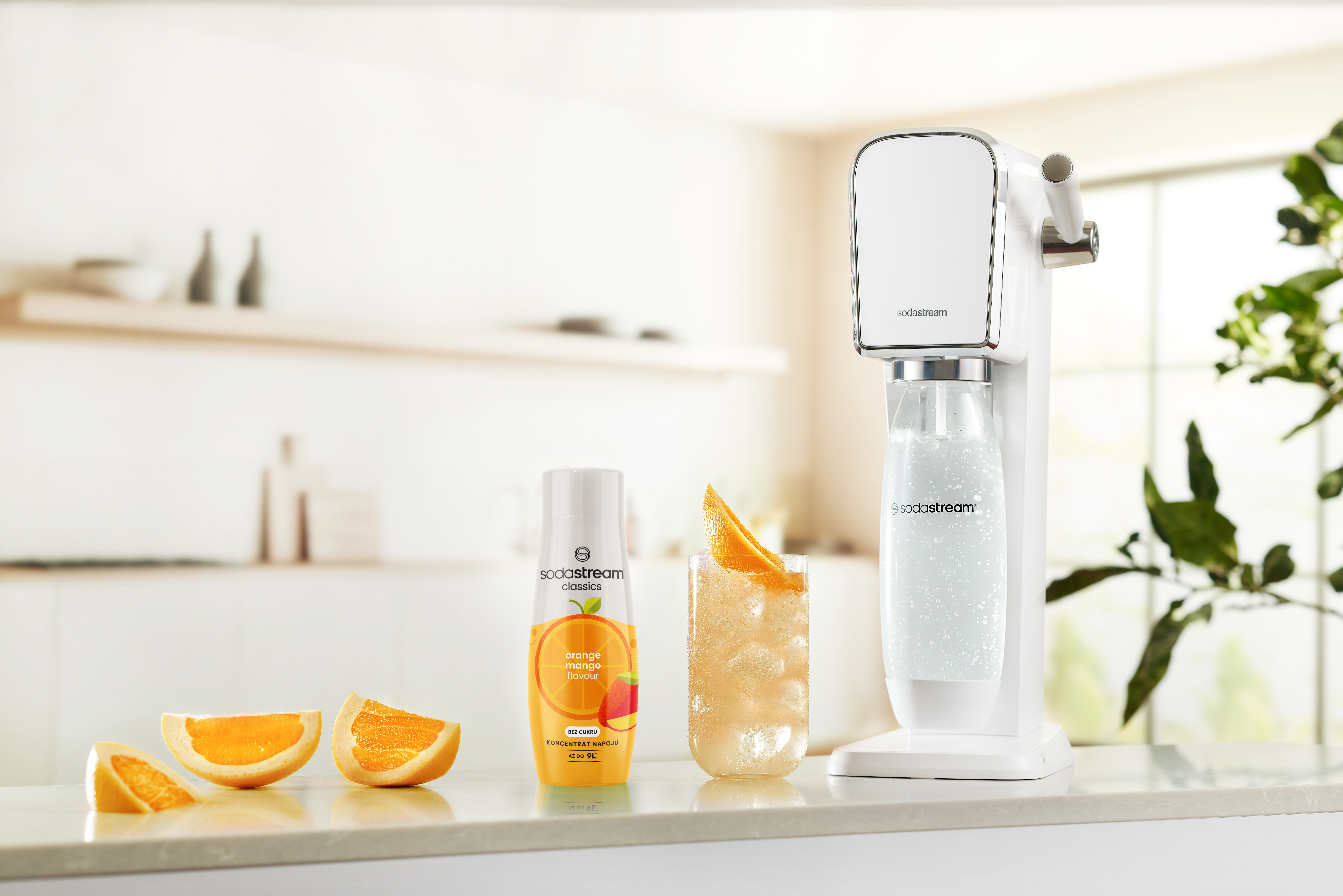 Maszyna SodaStream, plastry pomarańczy, napój i butelka na blacie. Tło to kuchnia.