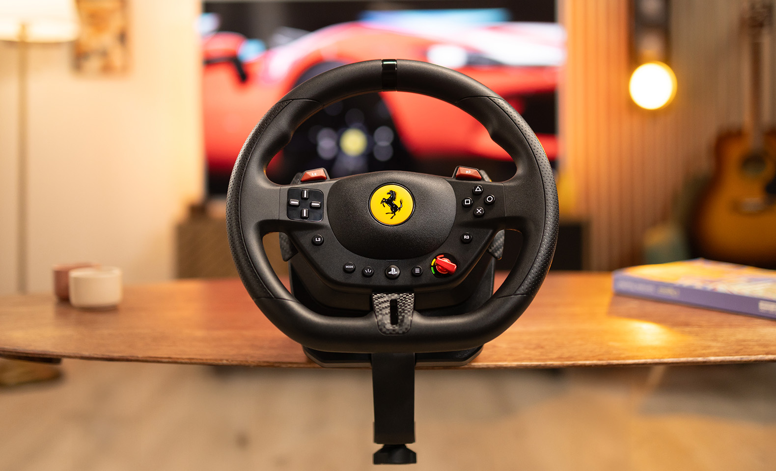 Volant noir Ferrari avec logo jaune. Boutons rouges, sur table en bois, avec fond d'écran flou.