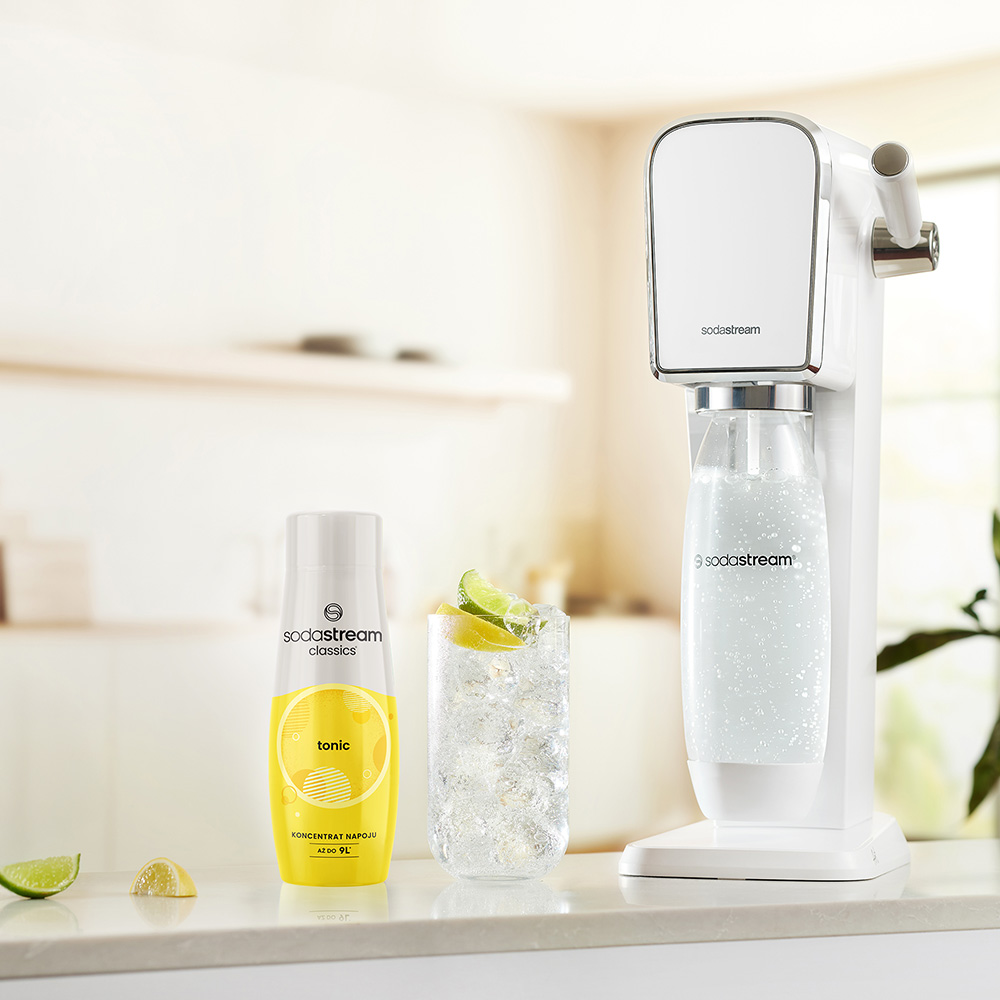 Białe urządzenie SodaStream ze szklanką toniku, butelką syropu tonikowego oraz plasterkami limonki i cytryny.