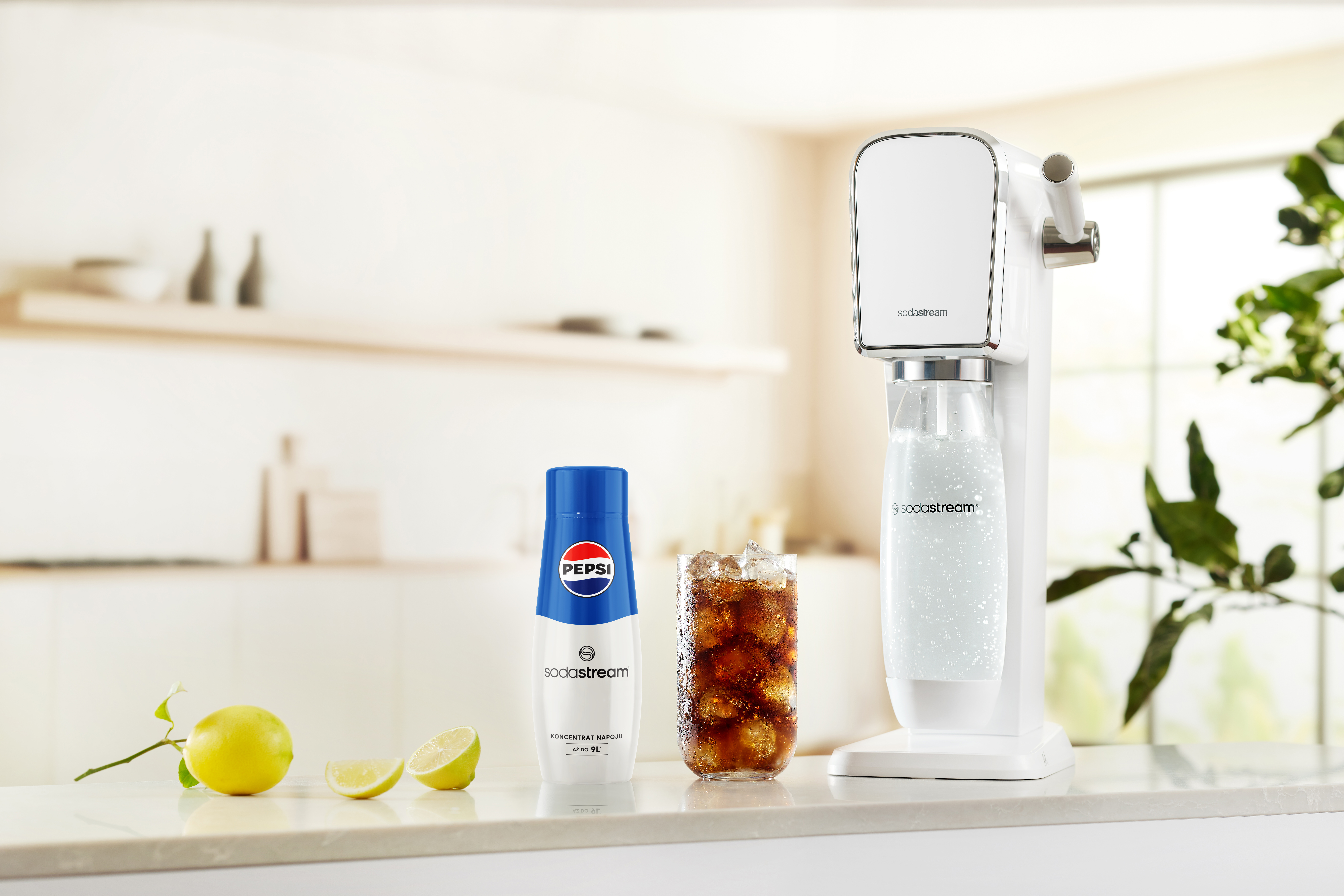 Maszyna SodaStream z butelką Pepsi, szklanką sody i cytrynami na blacie.