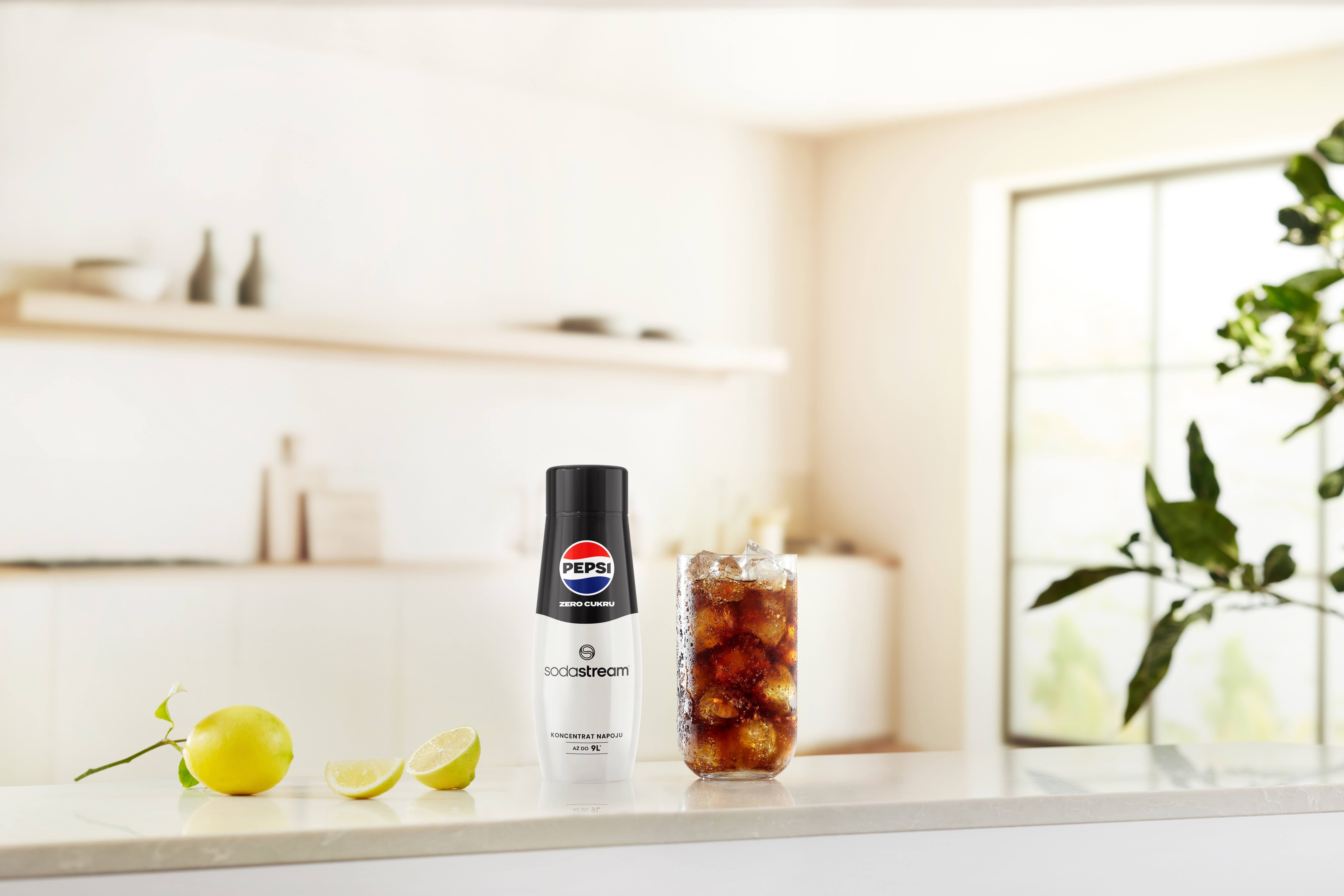 Butelka Pepsi i szklanka coli z lodem stoją na blacie z cytrynami. W tle okno i liście.