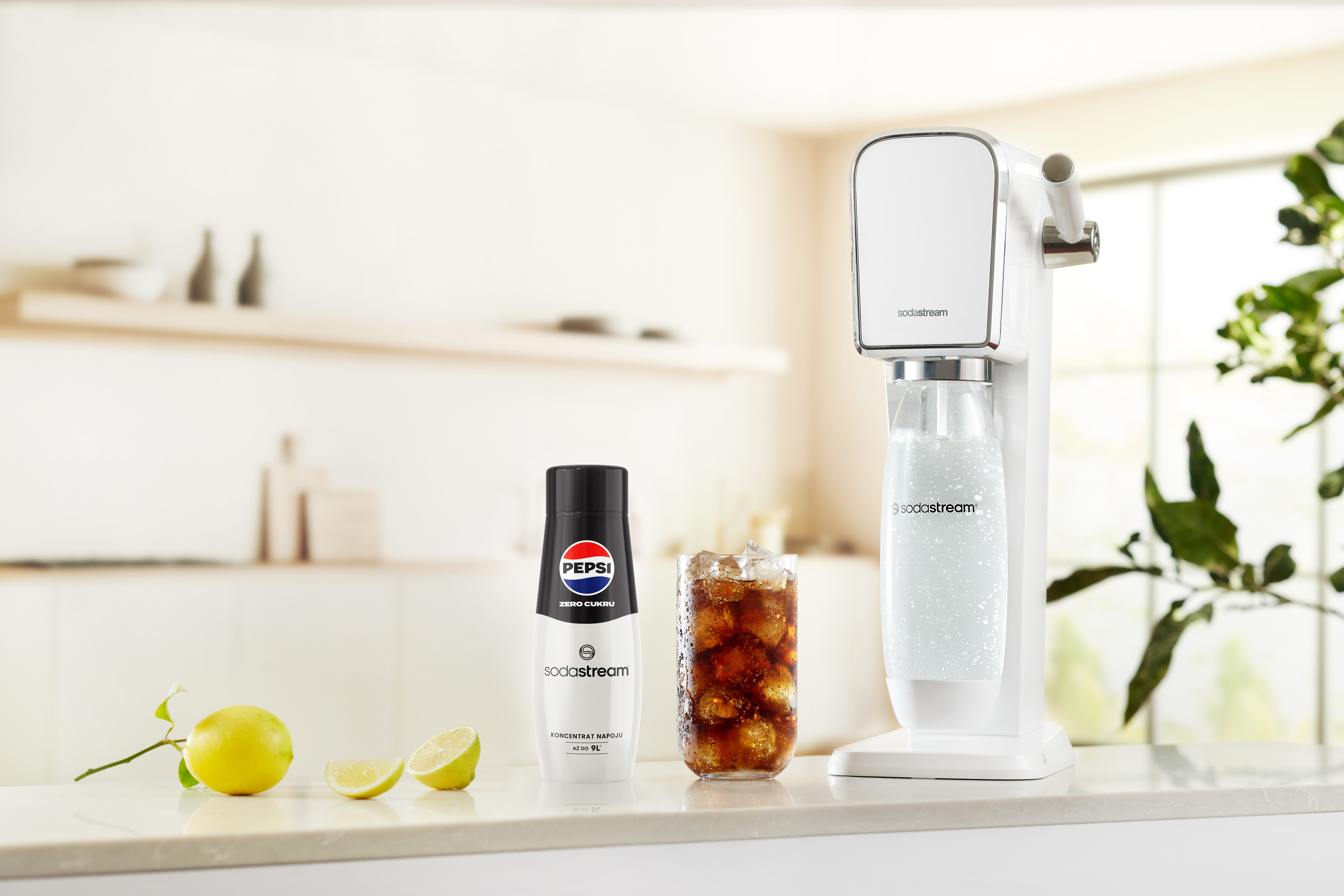 Automat SodaStream, butelka Pepsi, szklanka coli, cytryny i zieleń na białym blacie, jasne tło.