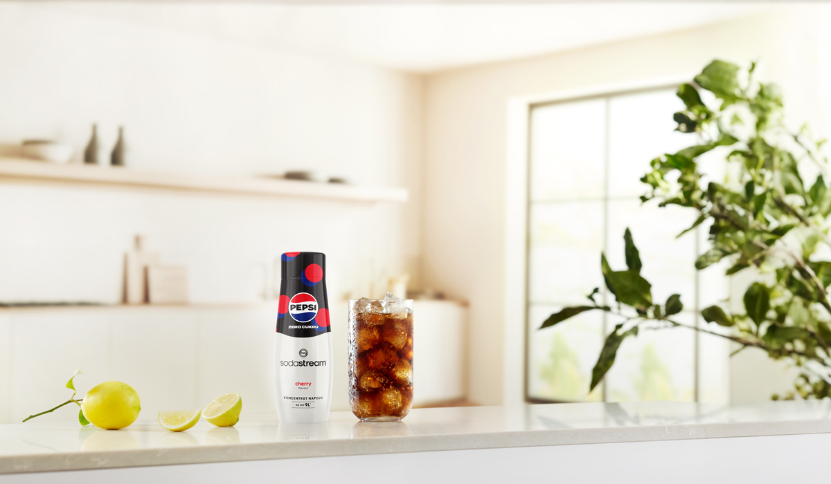 Butelka Pepsi SodaStream i szklanka coli z lodem stoją na blacie. Cytryny i roślina w tle.