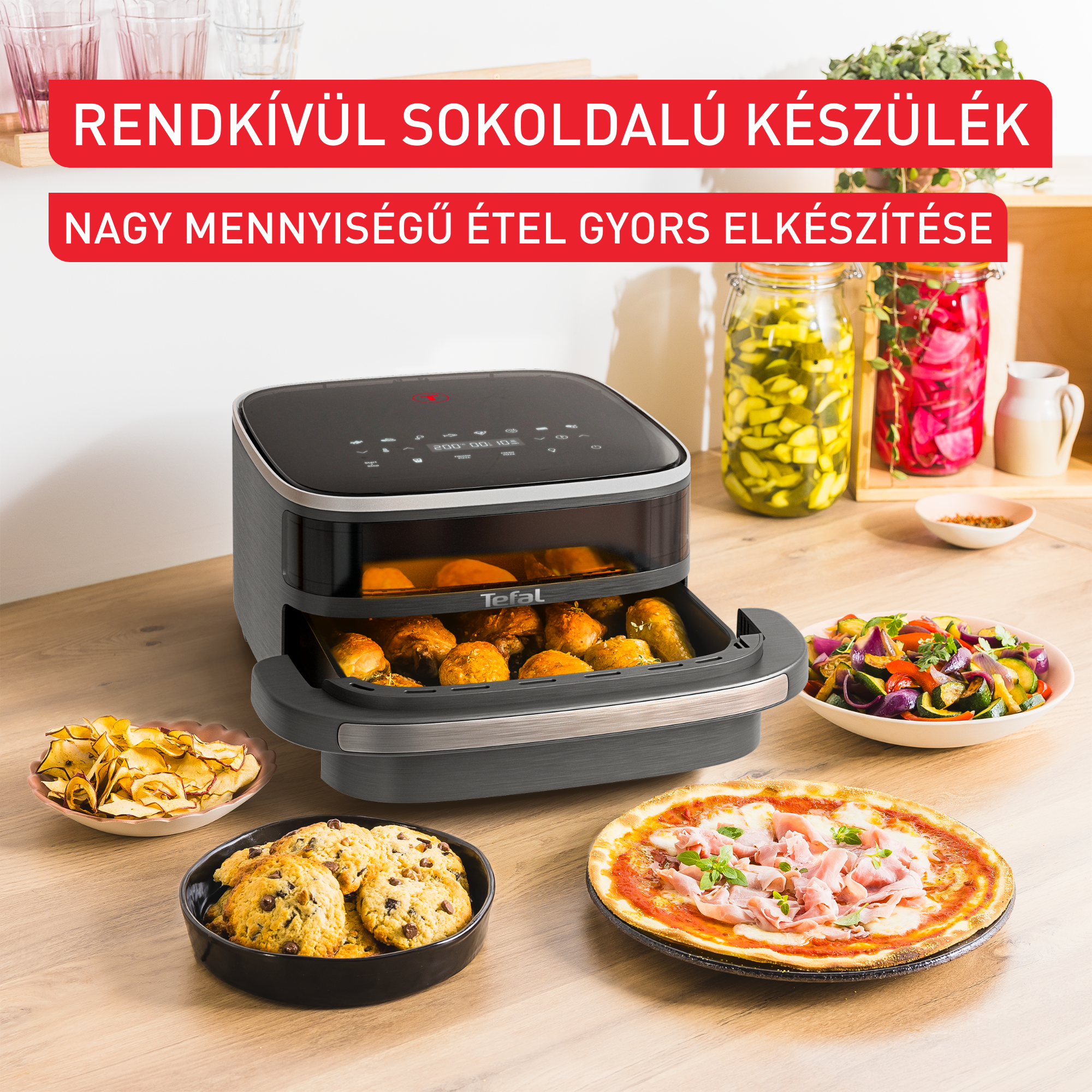 Egy air fryer sült ételekkel. Pizza, süti, chips és zöldségek az asztalon. Savanyúságos üvegek a háttérben.