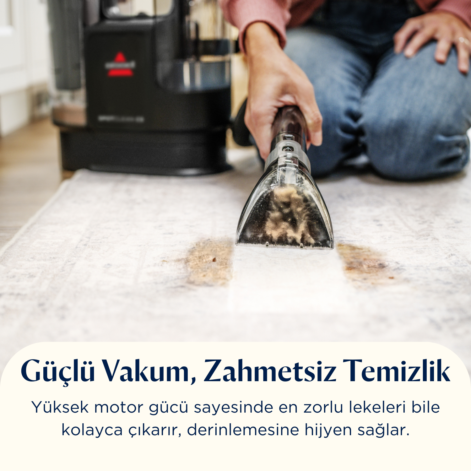 Bir kişi halıyı bir temizleme aracıyla temizliyor. Halıda bir leke var. Temizleyici siyah ve gümüş rengi.