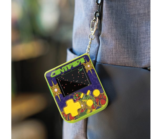 Przenośna gra Centipede na breloczku jest przymocowana do szarego paska plecaka. Gra ma ekran i kolorowe grafiki.