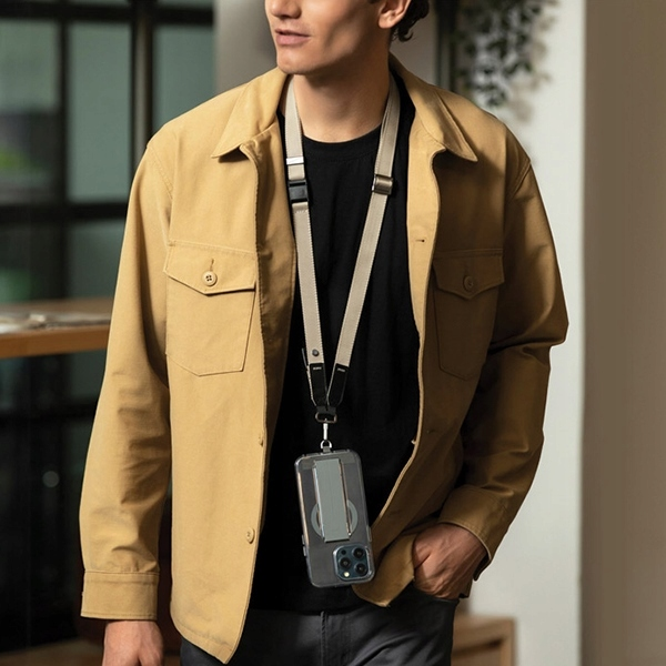 Mężczyzna w beżowej kurtce i czarnym t-shircie trzymający telefon z smyczą. Telefon jest w przezroczystym etui.