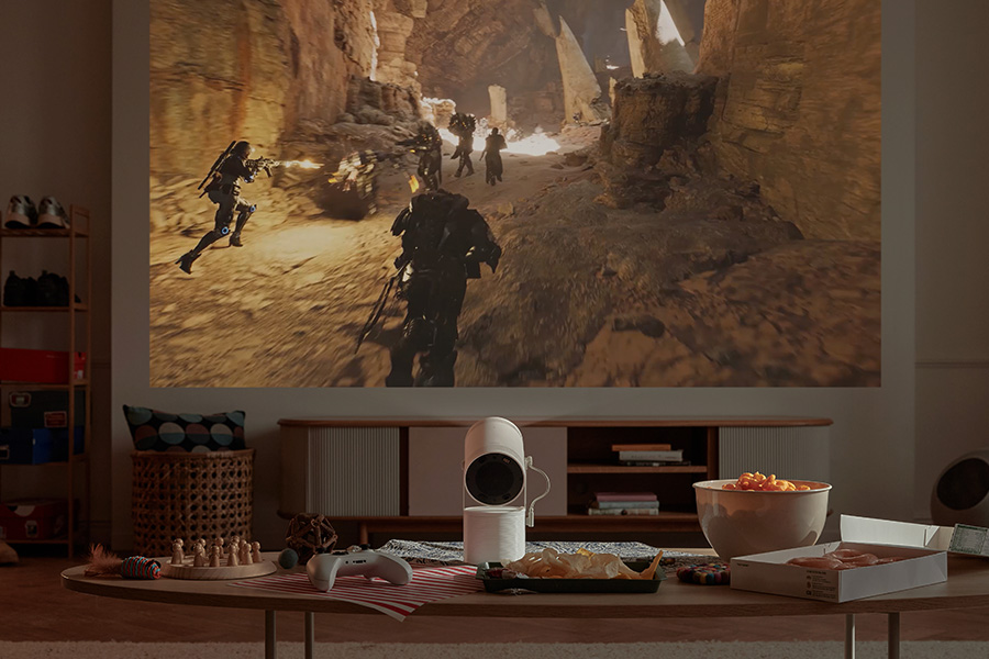 Eine Wohnzimmerszene mit einem projizierten Videospiel an der Wand. Ein Projektor steht auf dem Tisch mit Snacks und einem Gamepad.