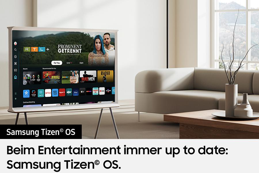 Ein weißer Fernseher zeigt Streaming-Inhalte. Sofa und Tisch stehen in einem hellen Wohnzimmer. Text: Samsung Tizen OS.