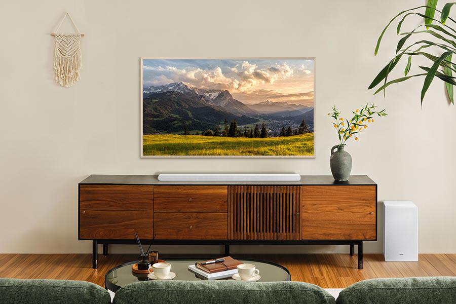 Wohnzimmer mit Fernseher, der eine Berglandschaft zeigt. Holzschrank, Couchtisch und grünes Sofa. Eine Pflanze und Dekoration.