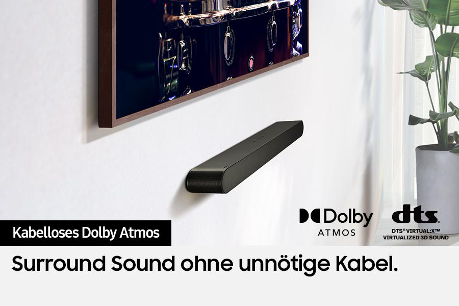 Eine schwarze Soundbar ist unter einem Fernseher an einer weißen Wand montiert. Der Text lautet 'Kabelloses Dolby Atmos Surround Sound'.
