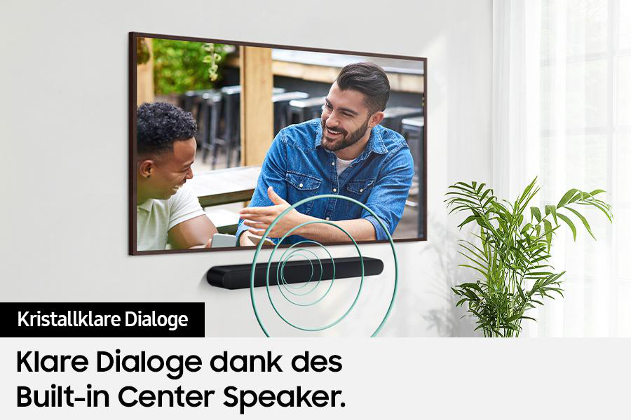 Zwei Männer lachen vor einem Fernsehbildschirm, eine Soundbar darunter. Rechts eine Pflanze. Text: Klarer Dialog dank eingebautem Center-Lautsprecher.