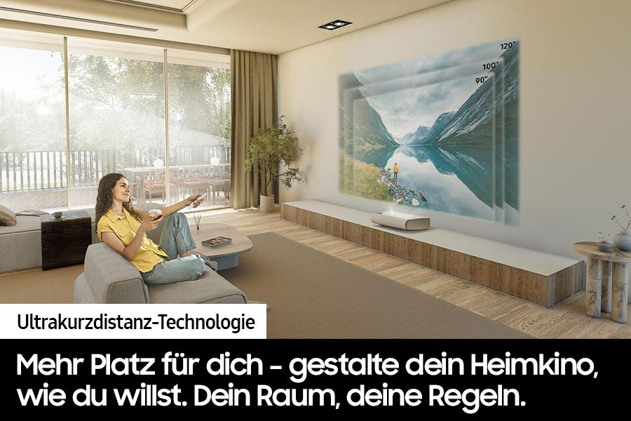 Eine Frau sitzt auf einer Couch und hält eine Fernbedienung. Ein Projektor zeigt eine Seeszene. Text: Ultrakurzdistanz-Technologie.
