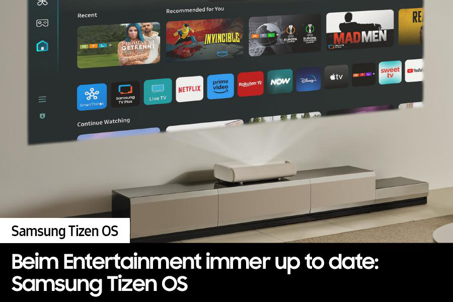 Ein Projektor projiziert auf einen Bildschirm mit Apps. Unter dem Bildschirm befindet sich ein Schrank mit einem Projektor. Text: 'Samsung Tizen OS'.