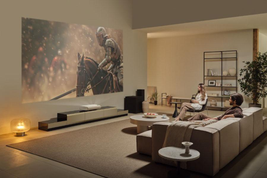 Wohnzimmer mit Filmprojektion eines Ritters auf einem Pferd. Zwei Personen sitzen auf einem Sofa, eine weitere auf einem Stuhl.