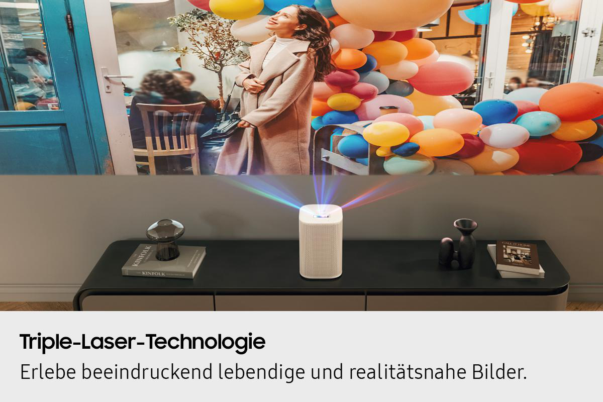 Eine Frau blickt zu Ballons auf. Ein Projektor sendet farbiges Licht aus. Objekte auf einem Tisch vor einer Wand.