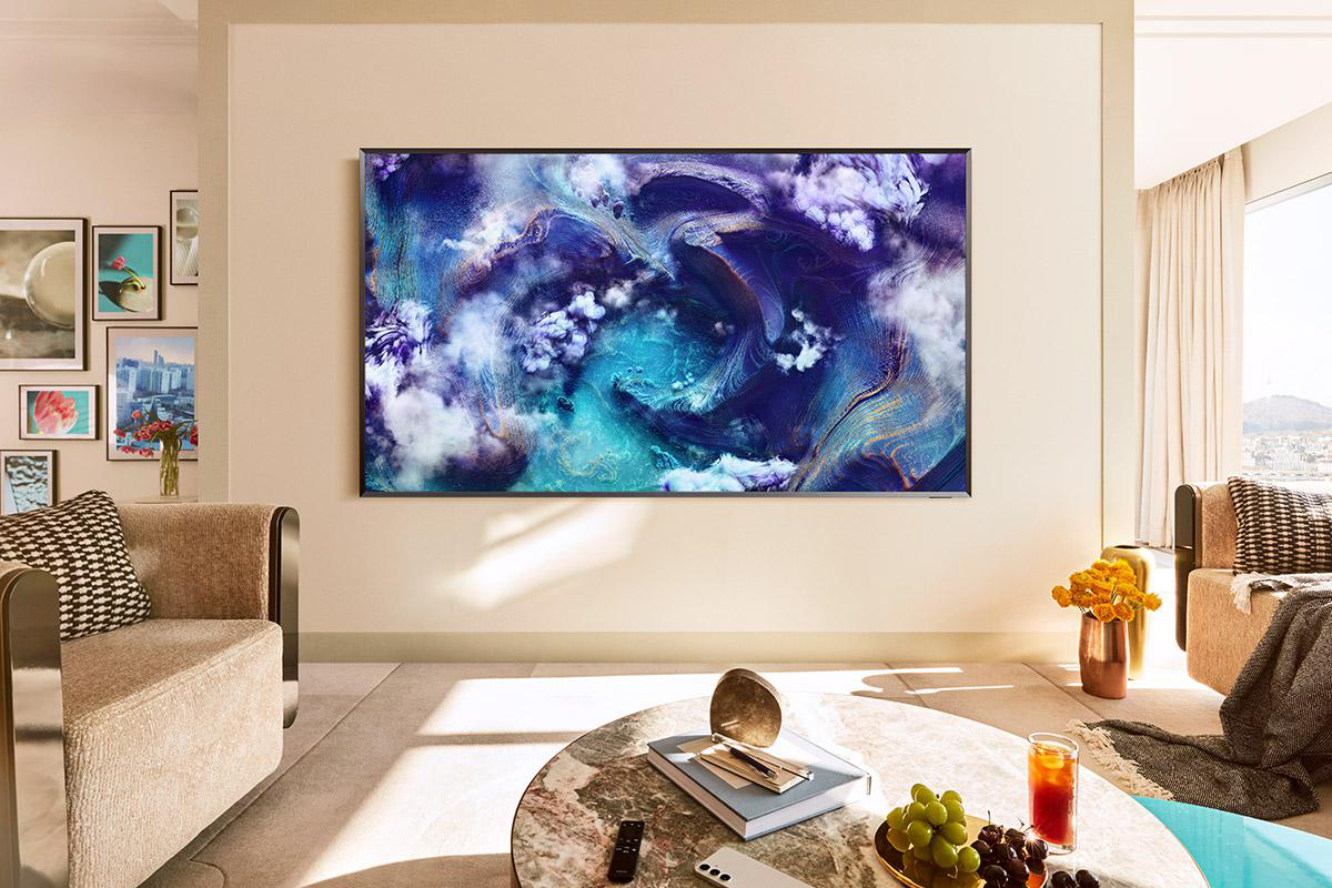 Wohnzimmer mit großem Fernseher mit abstrakter Kunst. Es gibt ein Sofa, einen Couchtisch und ein Fenster mit Stadtblick.