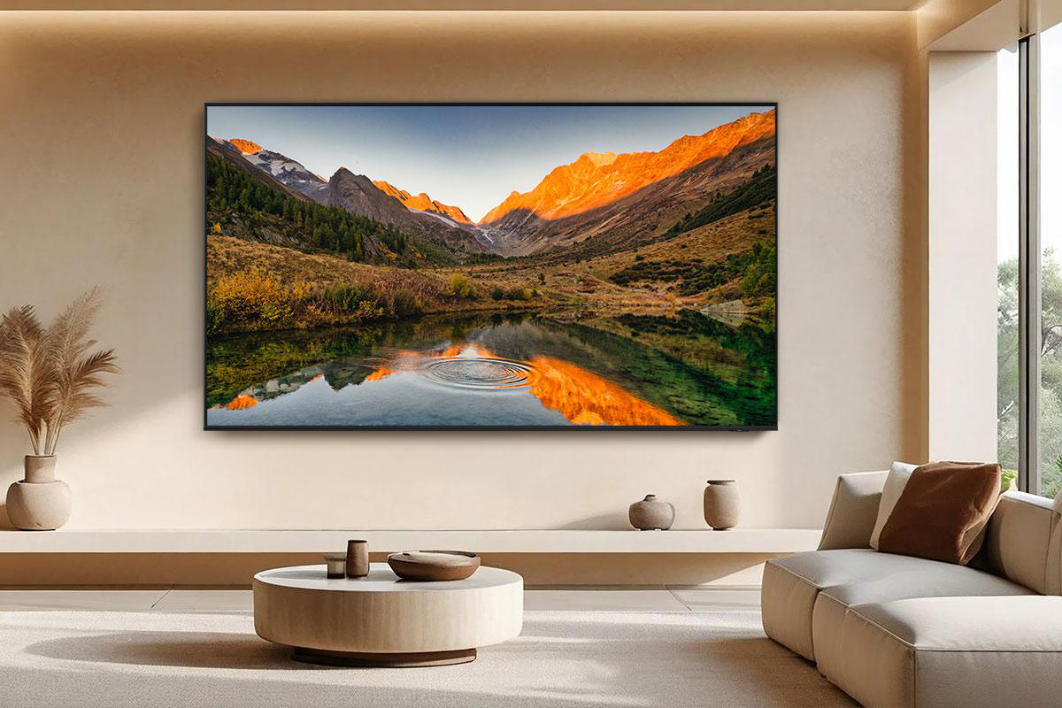 Ein großer Fernseher zeigt eine Berglandschaft mit einem See, der Berge und Himmel widerspiegelt. Ein Wohnzimmer mit Sofa und Tisch.