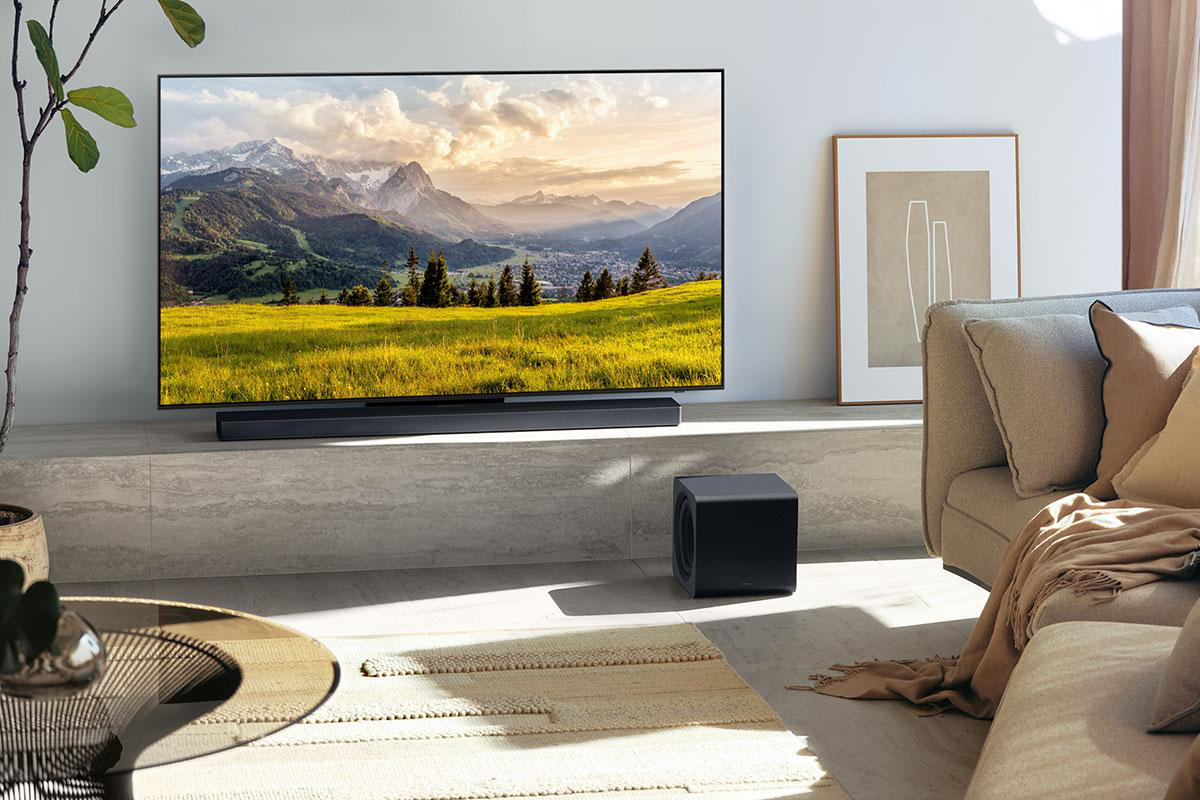 Wohnzimmer mit TV, der Berge zeigt, Soundbar, Subwoofer, Couch und Couchtisch.