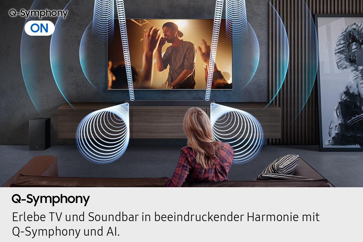 Eine Frau sieht fern. Unter dem Fernseher befindet sich eine Soundbar. An der Seite befinden sich Lautsprecher. Die Szene spielt in einem Wohnzimmer.
