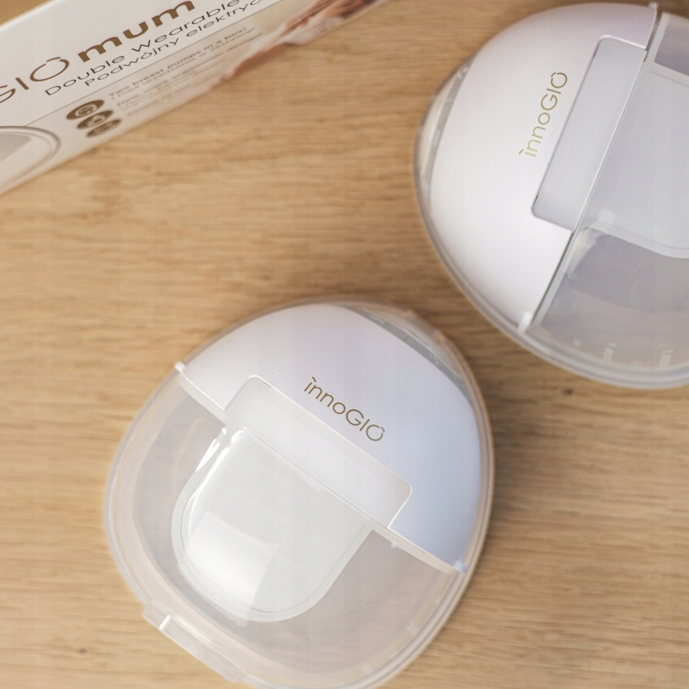 Dwie białe laktatory InnoGIO na drewnianej powierzchni. Częściowo widoczne pudełko w tle.