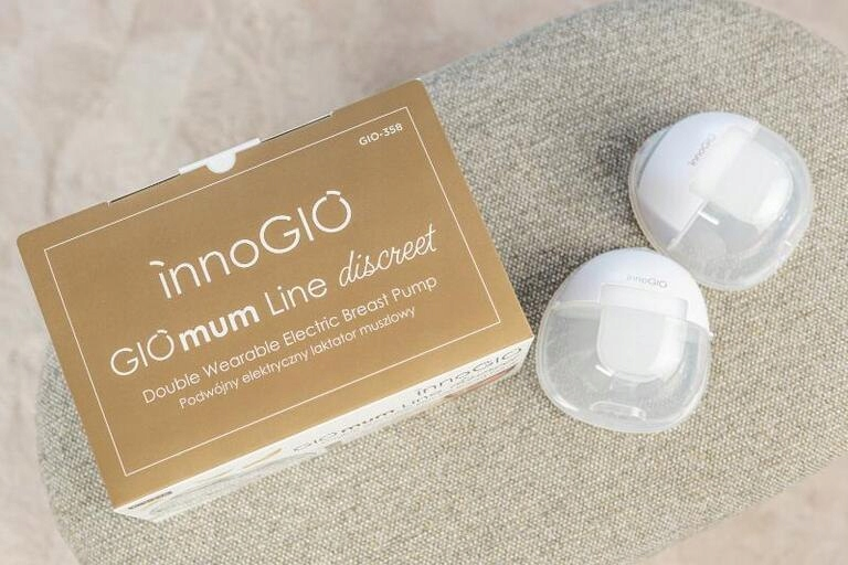 Pudełko laktatora InnoGIO i dwie białe pompy na szarej powierzchni. Na pudełku napis 'GIOmum Line discreet'.