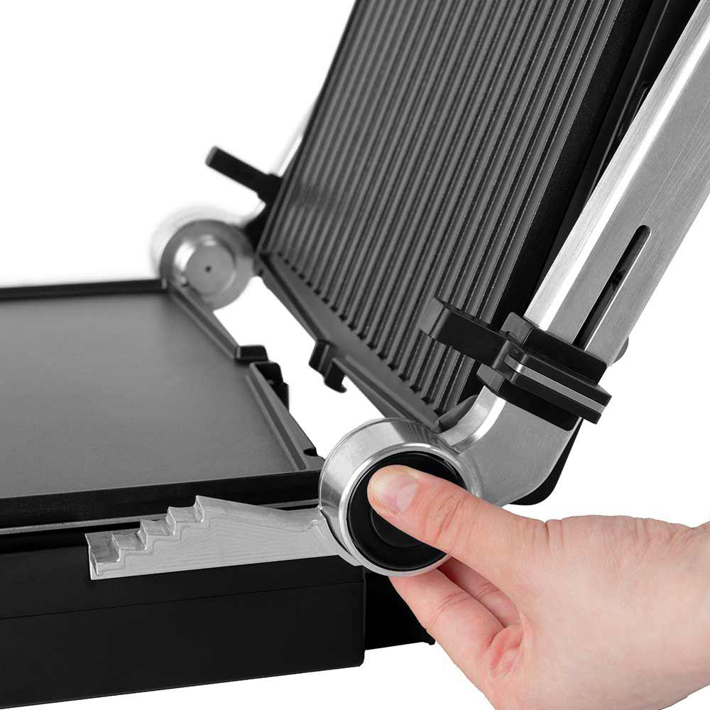 Eine Hand bedient eine Panini-Presse. Die Presse ist geöffnet und zeigt den Grill und die flache Oberfläche. Sie ist silber, schwarz und hat einen Griff.