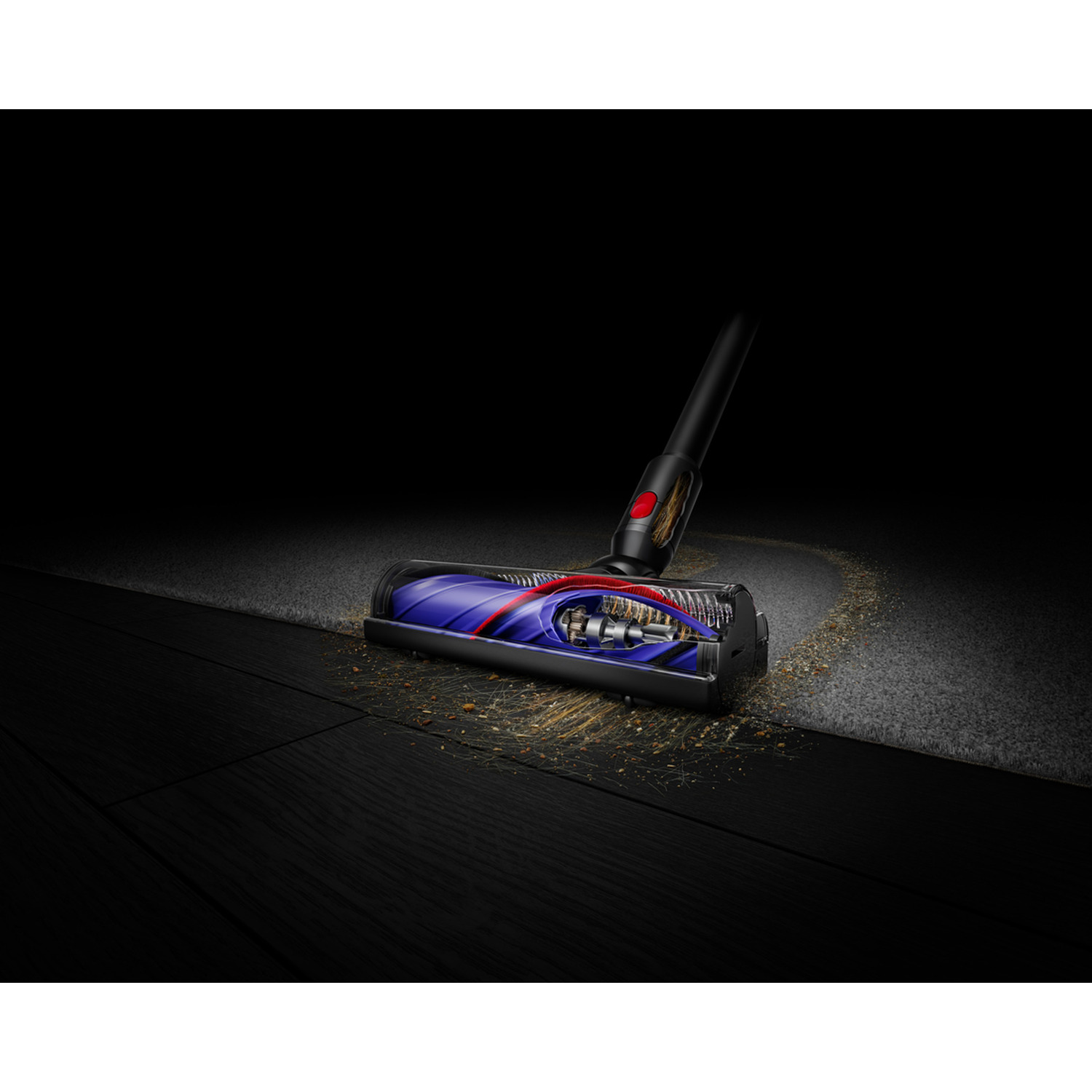 Vacuum cleaner head cleaning carpet, showing internal parts. Dark wood floor in the foreground, black background.