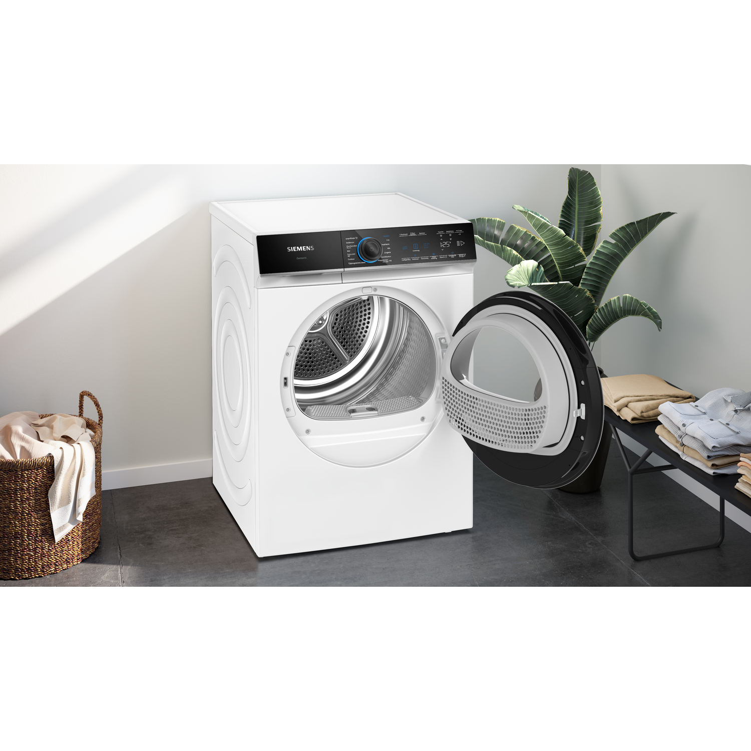 A white Siemens dryer with an open door, a wicker basket, and a plant stand with folded clothes.