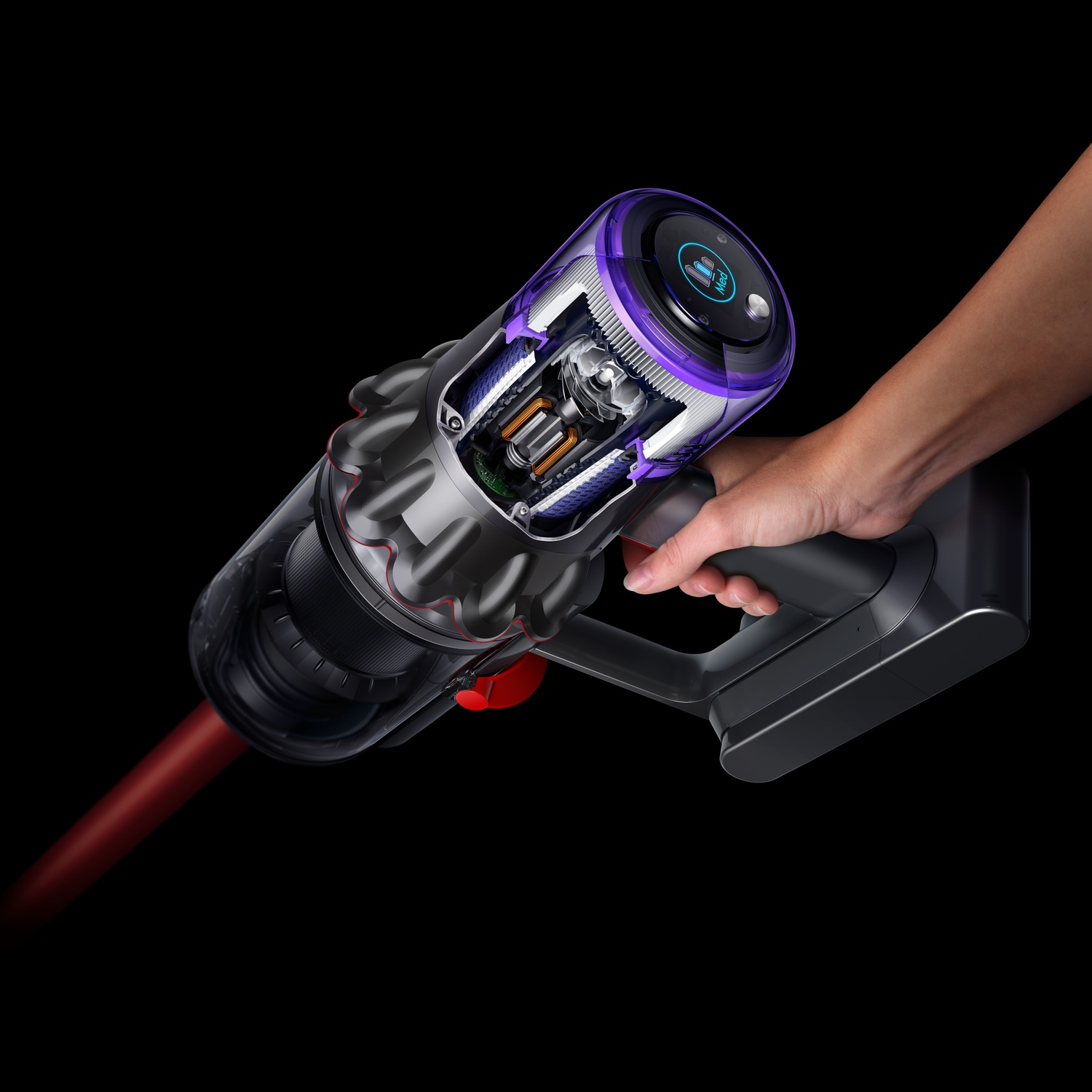 Een hand houdt een doorgesneden Dyson stofzuiger vast op een zwarte achtergrond. De stofzuiger heeft een paarse bovenkant, rode knop en transparante onderdelen.