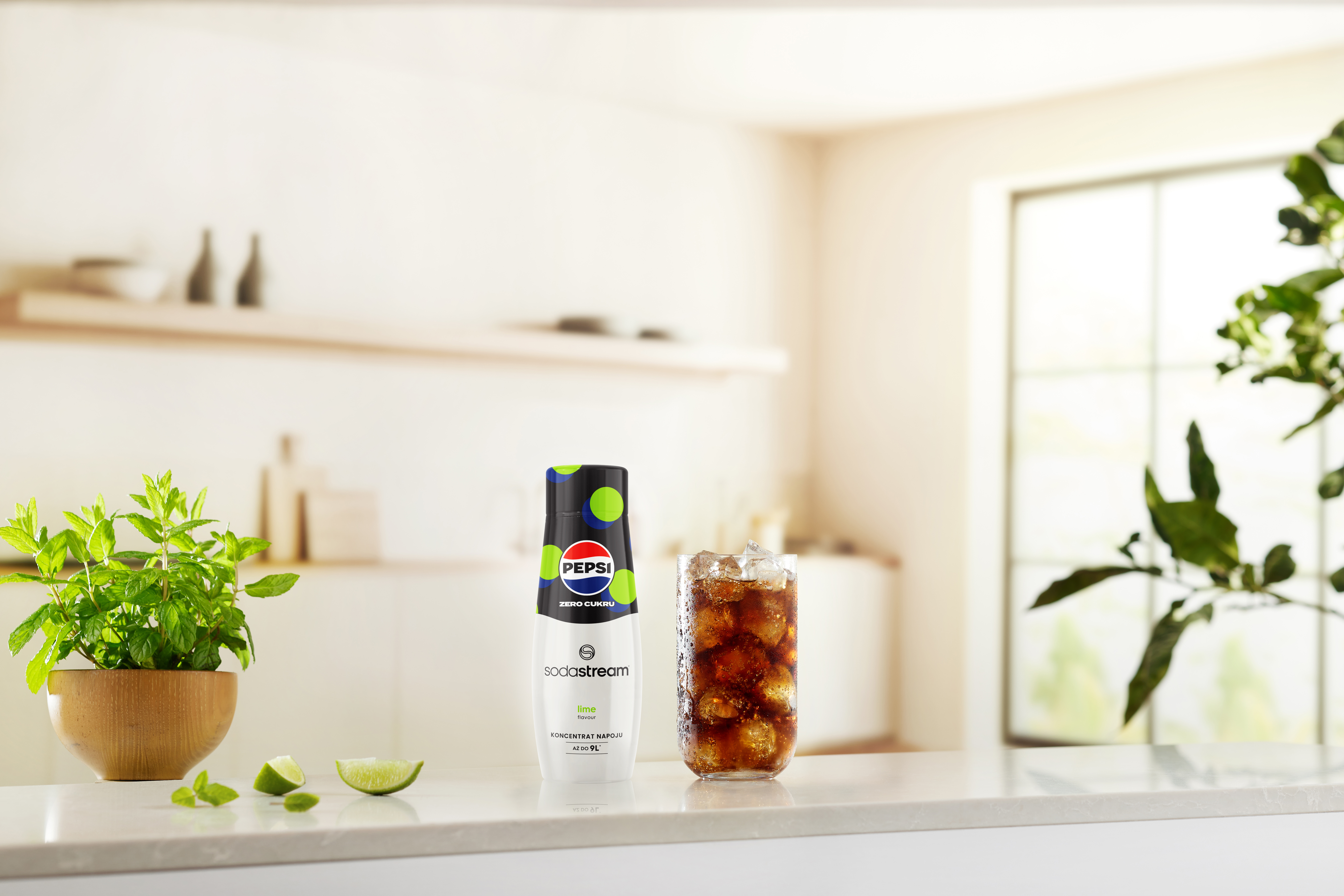 Scena kuchenna z butelką Pepsi, szklanką coli, miętą i limonkami na białym blacie. Tło: okno.