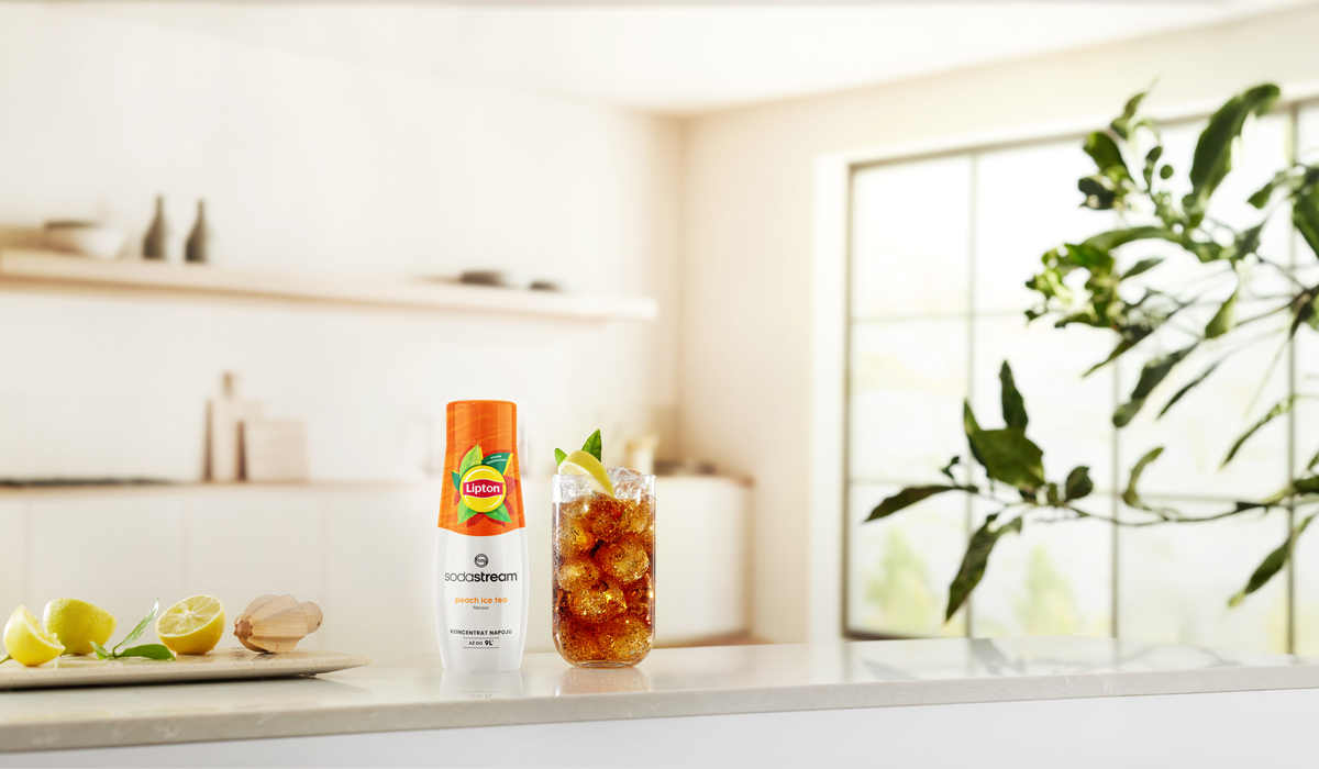 Szklanka mrożonej herbaty z plasterkiem cytryny i miętą, butelka herbaty mrożonej brzoskwiniowej Lipton i cytryny na blacie.