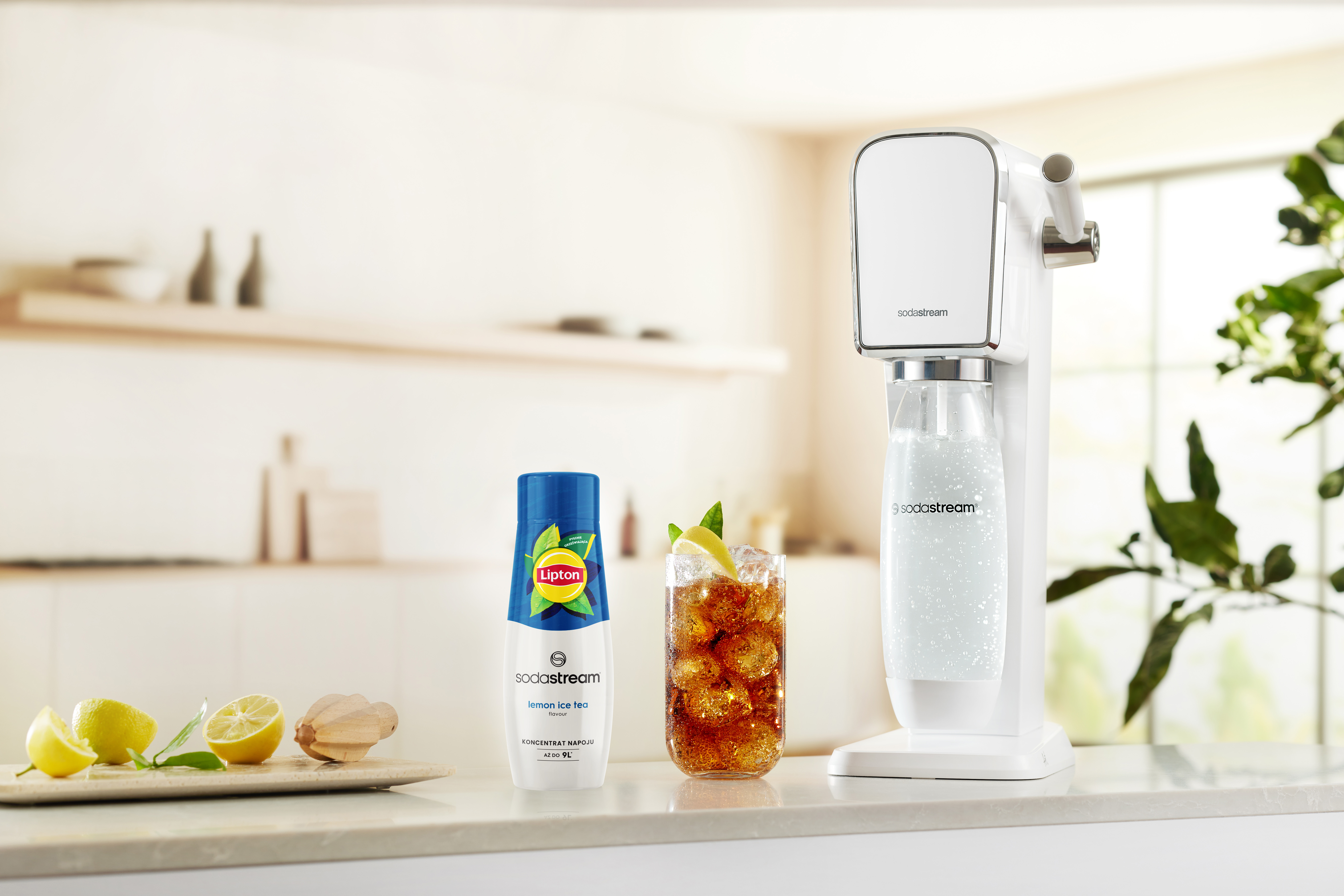 Maszyna SodaStream, szklanka mrożonej herbaty i butelka mrożonej herbaty cytrynowej Lipton. Obecne są również cytryny i wyciskarka do owoców.