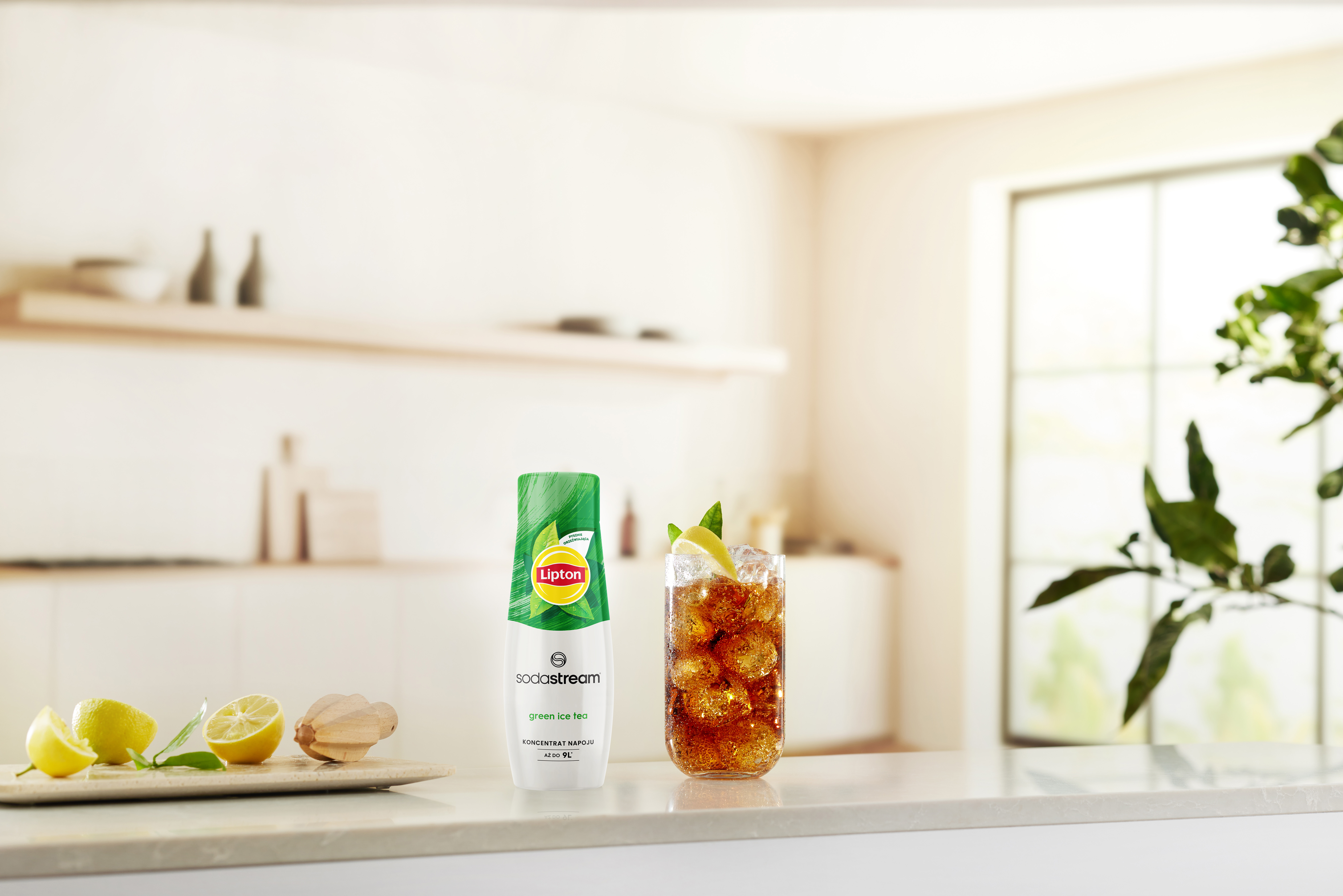 Na blacie butelka Lipton SodaStream, szklanka mrożonej herbaty i połówki cytryny. W tle kuchnia.