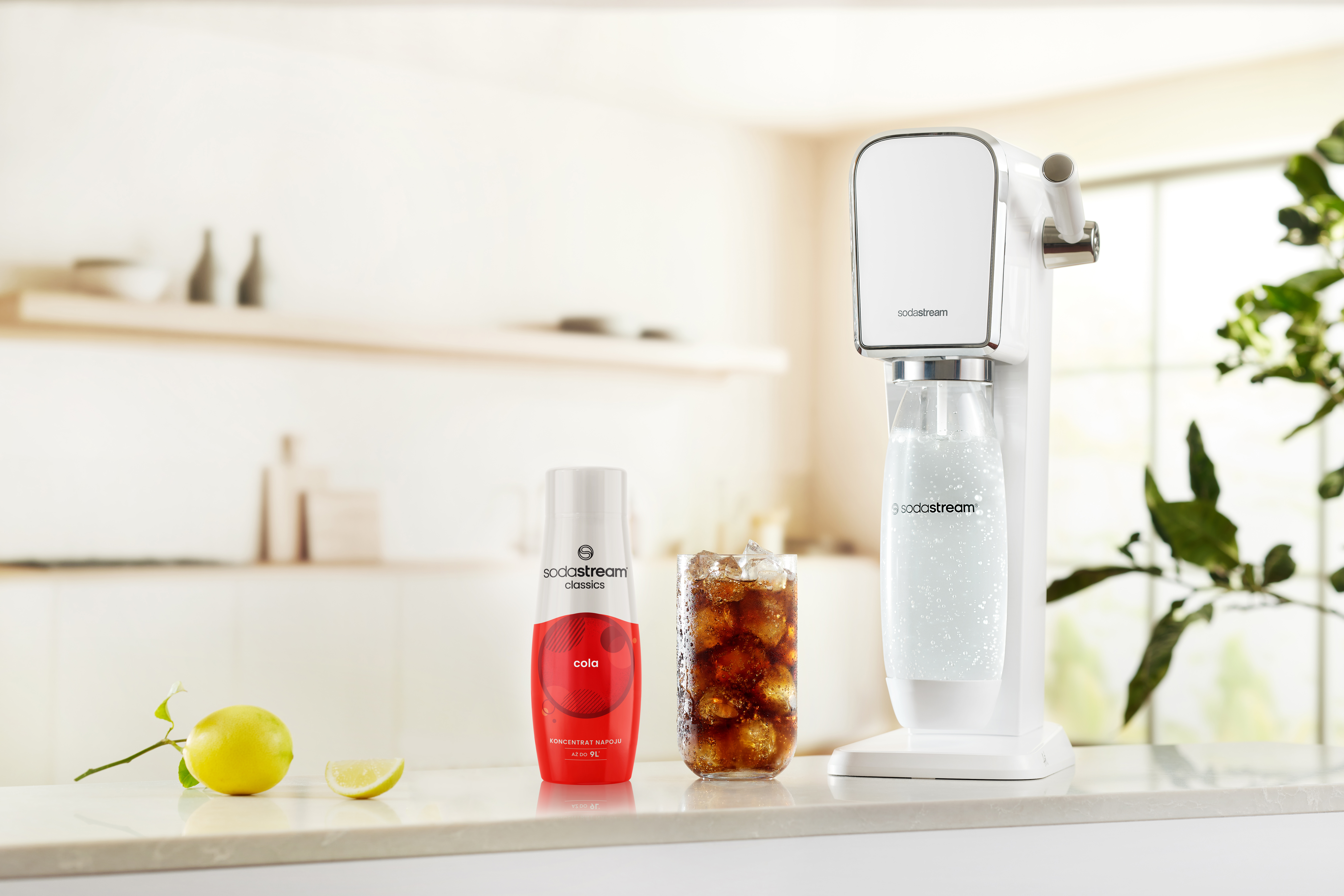 Maszyna SodaStream, butelka coli, szklanka coli i cytryna na blacie.