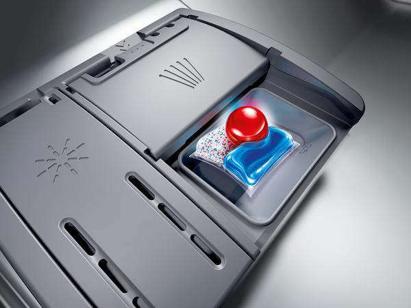 Geschirrspülmittelkammer mit einem roten und blauen Waschmittelpod und einer Tablette.