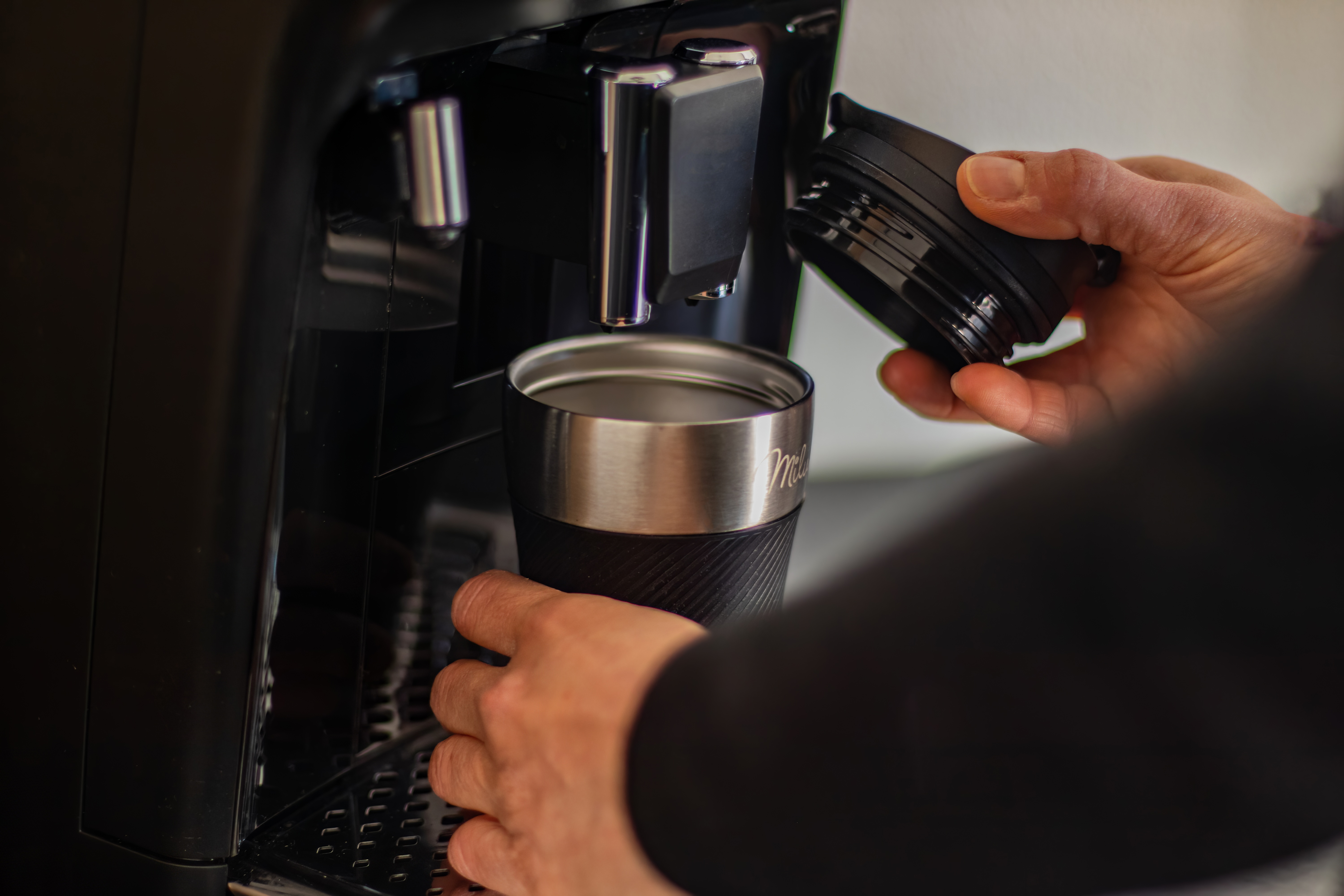 Eine Person benutzt eine Kaffeemaschine und setzt einen Deckel auf einen Edelstahl-Reisebecher.
