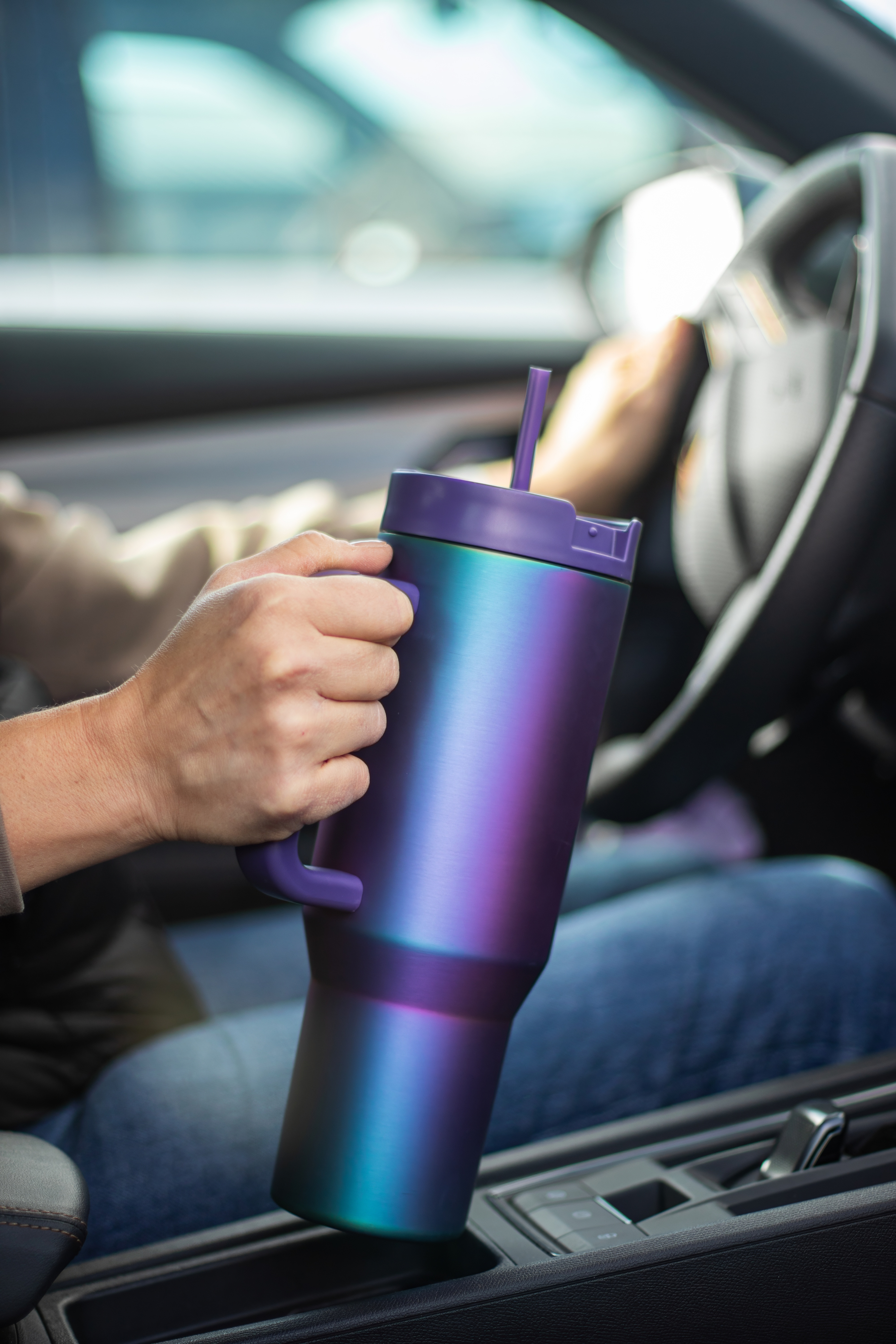 Eine Person hält einen violett-türkisfarbenen Becher mit Strohhalm in einem Auto. Der Innenraum ist im Fokus.