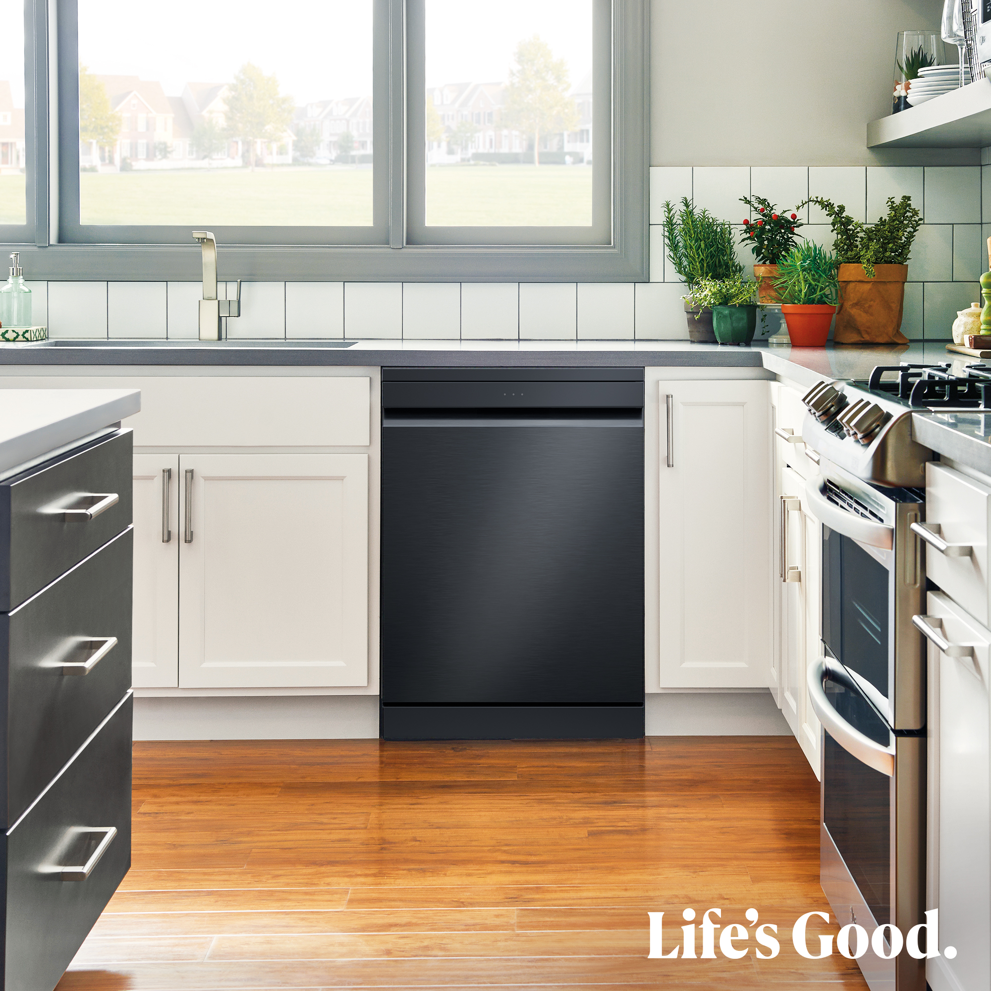 Cocina moderna con lavavajillas negro, gabinetes blancos y suelo de madera. Ventana con vista al vecindario. Texto Life's Good.