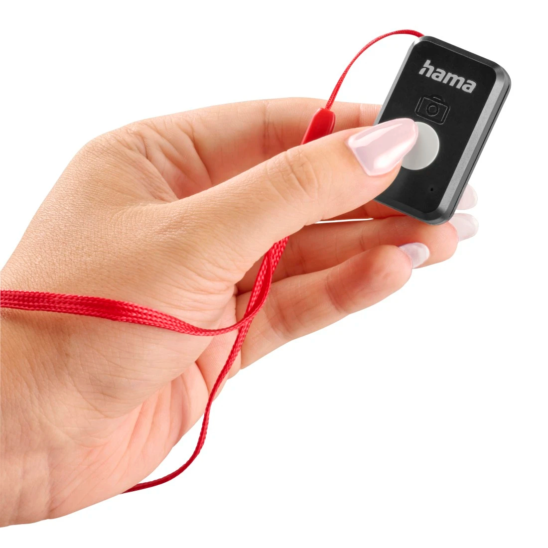 Dłoń trzyma czarny pilot Hama z białym przyciskiem i czerwonym sznurkiem. Paznokcie są pomalowane na jasnoróżowo.