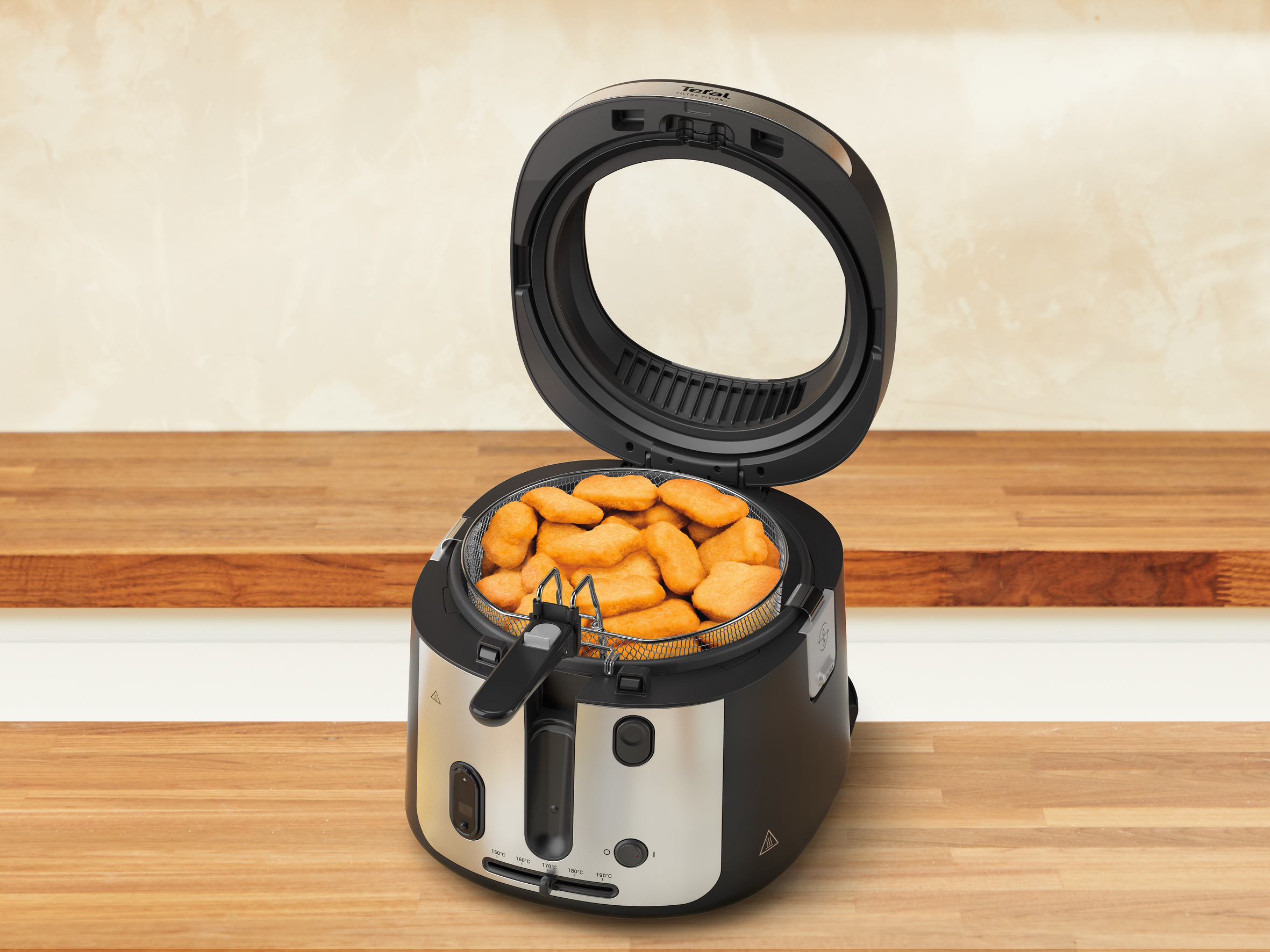 Egy nyitott Tefal fritőz csirkefalatokkal a kosárban. Fa felületen van.
