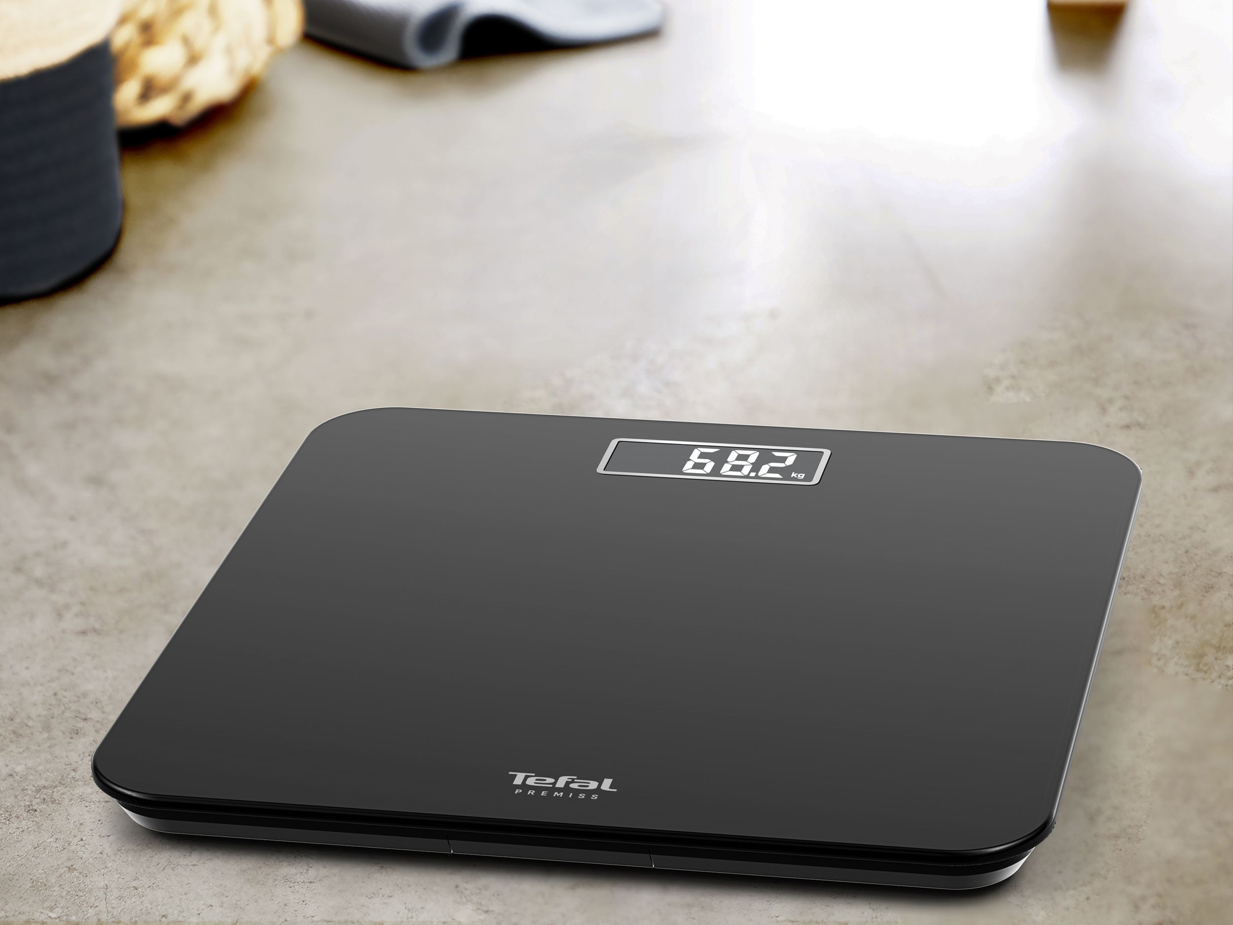 Egy fekete digitális fürdőszobamérleg 68,2 kg-ot mutat. A márka a Tefal Premiss. Világos felületen van.