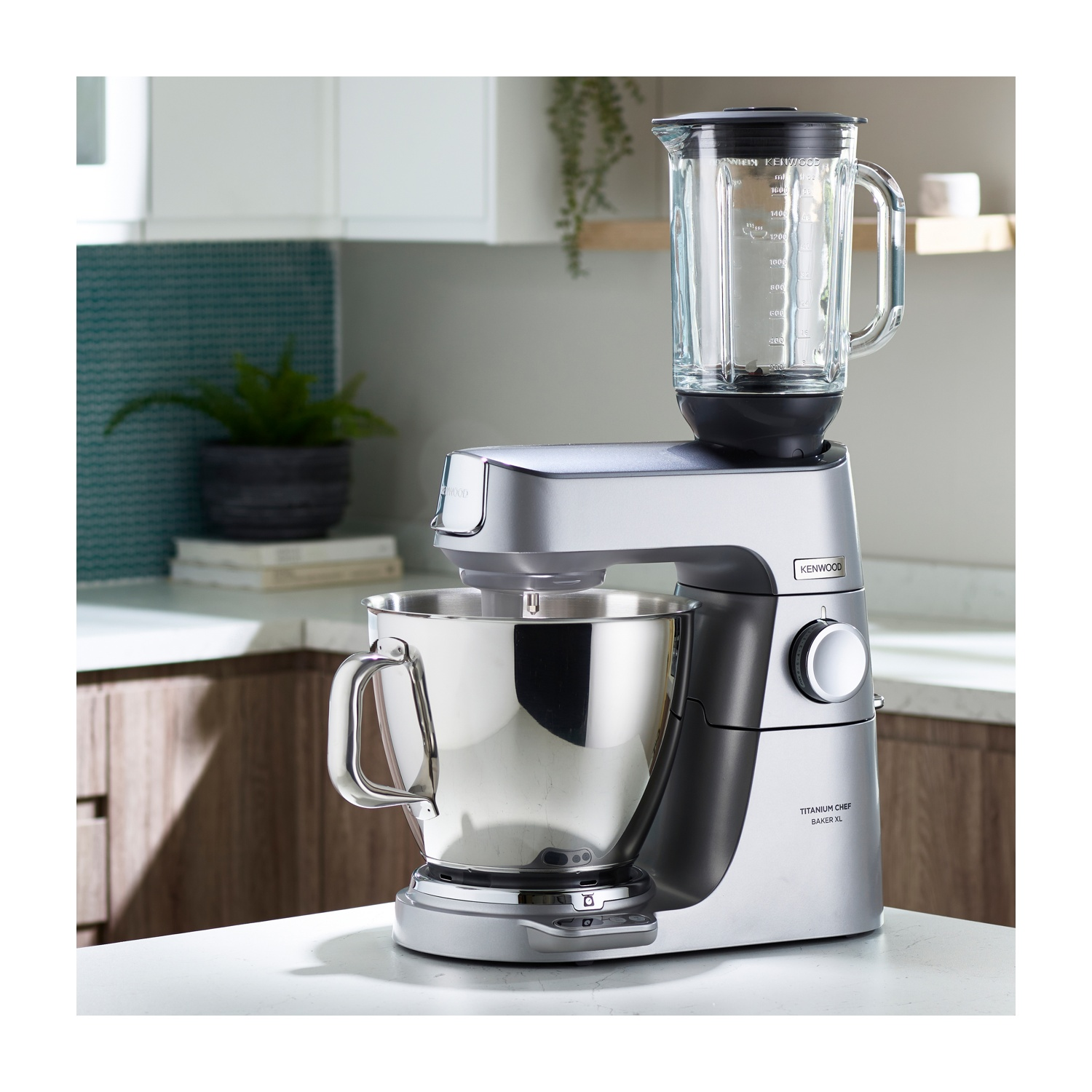 Una macchina da cucina argentata Kenwood Titanium Chef Baker XL con accessorio frullatore. Su una superficie bianca in ambiente cucina.