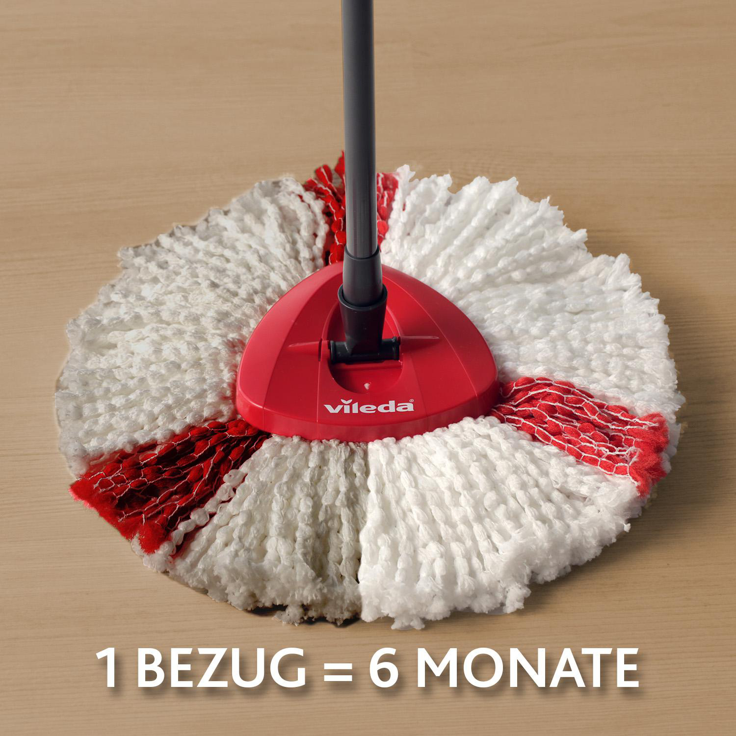 Ein roter und weißer Vileda-Wischmopp auf einer Holzoberfläche. Der Text unten lautet: 1 BEZUG = 6 MONATE.