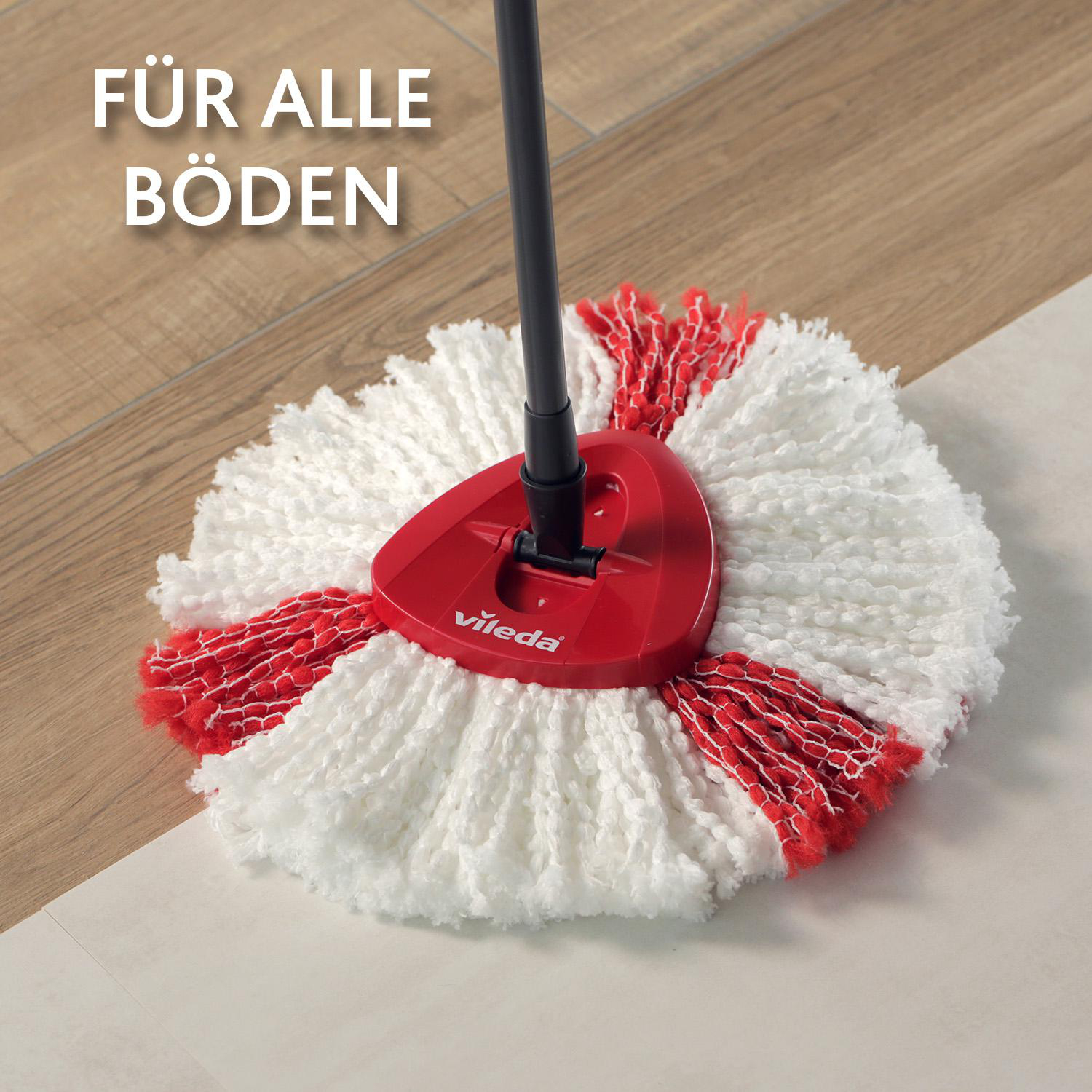 Ein Vileda-Wischmopp mit rotem Kopf und weißen und roten Wischmoppsträhnen auf Holz- und weißen Fliesenböden.