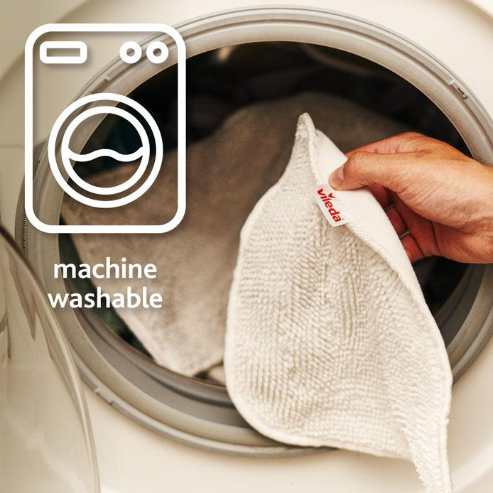 Eine Hand legt ein weißes Vileda-Tuch in eine Waschmaschine. Die Maschine zeigt ein Symbol für Maschinenwäsche.