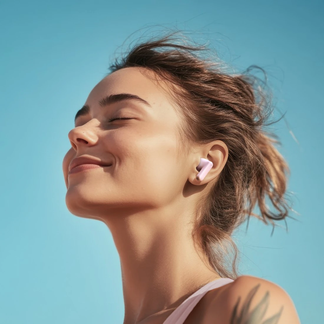 Egy nő csukott szemmel mosolyog, rózsaszín fülhallgatót visel. A haja a szélben lobog a ragyogó kék égbolttal szemben. Tetoválás látható a karján.