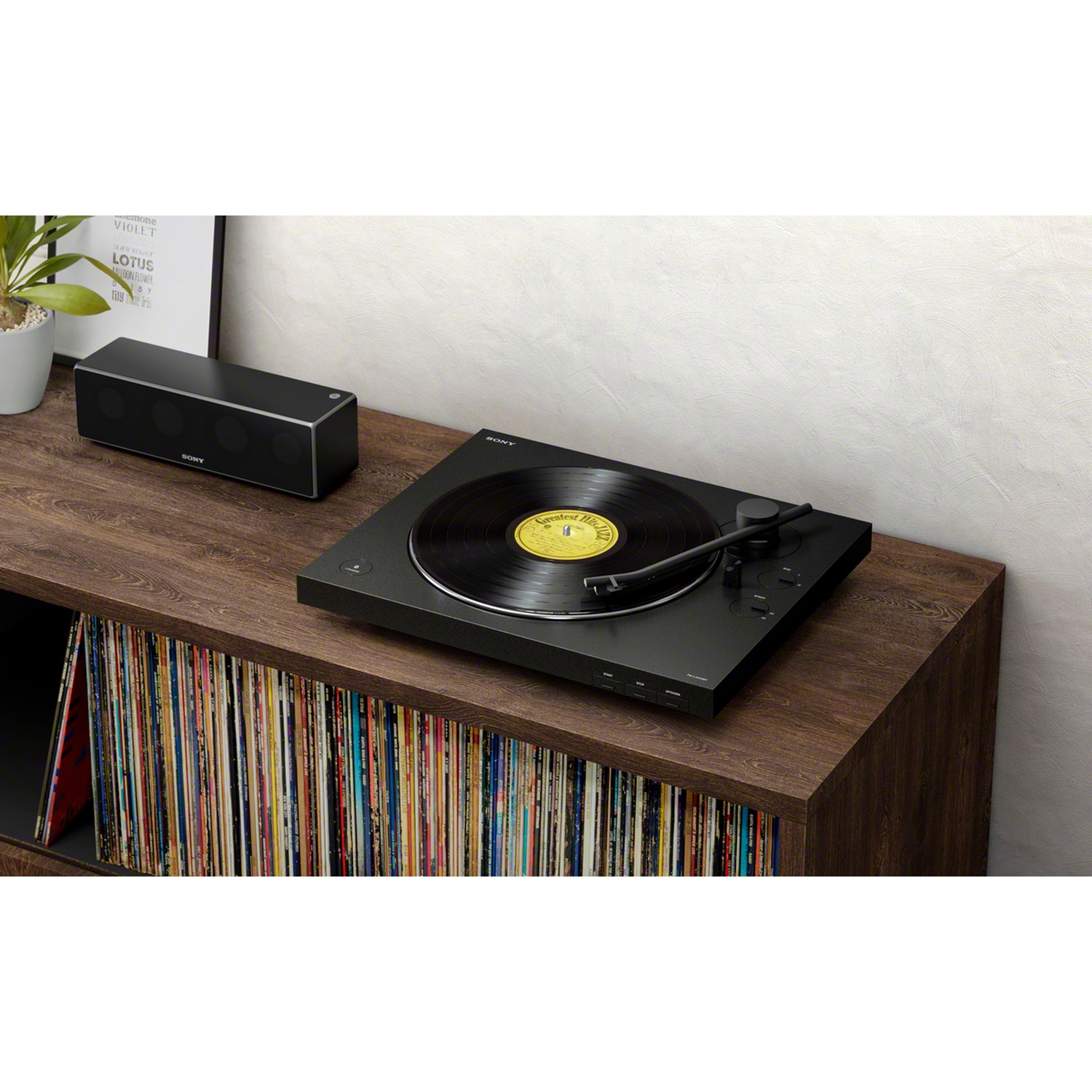 Un giradischi nero con un disco in vinile è su uno scaffale di legno, con un altoparlante, arte incorniciata e dischi sullo sfondo.