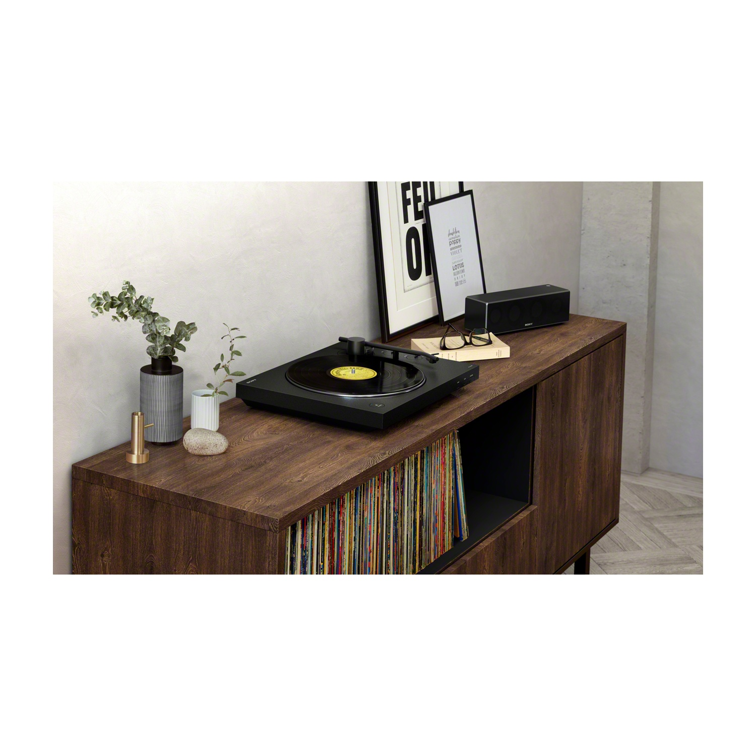 Un mobile in legno con giradischi, arte incorniciata, altoparlante e dischi all'interno. Un vaso con piante a sinistra.
