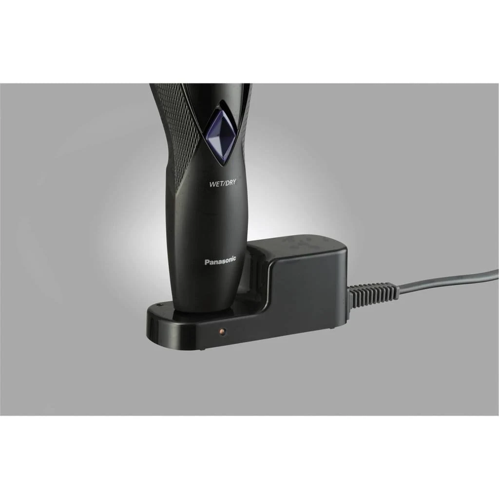 Una afeitadora eléctrica Panasonic negra en su base de carga. La afeitadora está etiquetada como 'WET/DRY'. El cargador tiene un cable de alimentación.